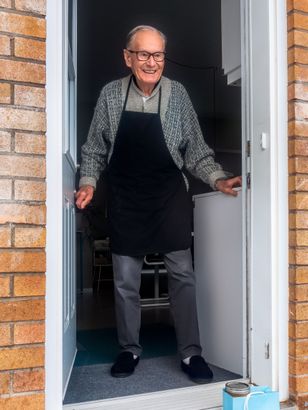 an elderly man in an apron is standing in a doorway .