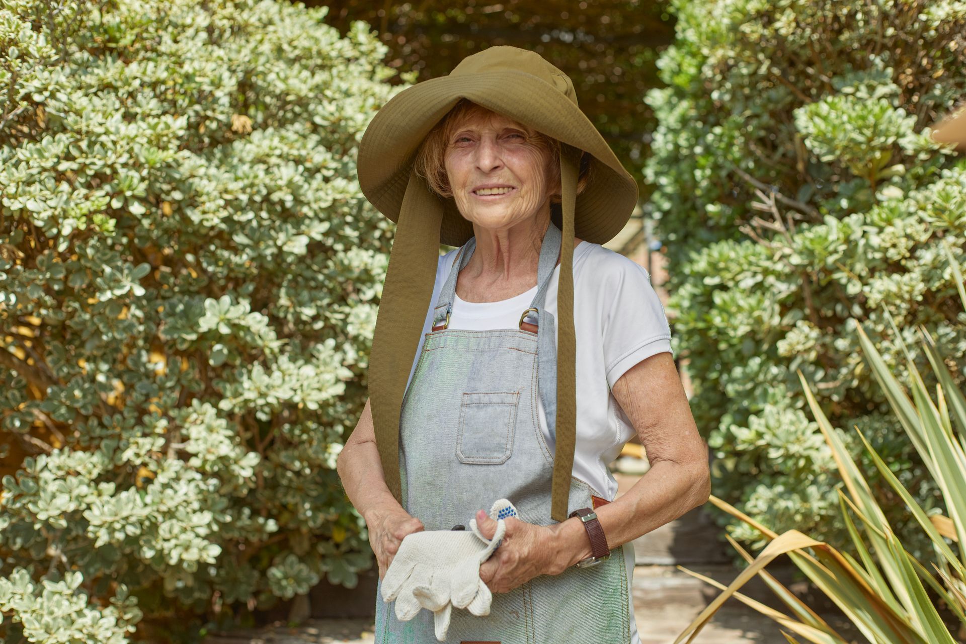an elderly woman wearing a hat and apron is standing in a garden .