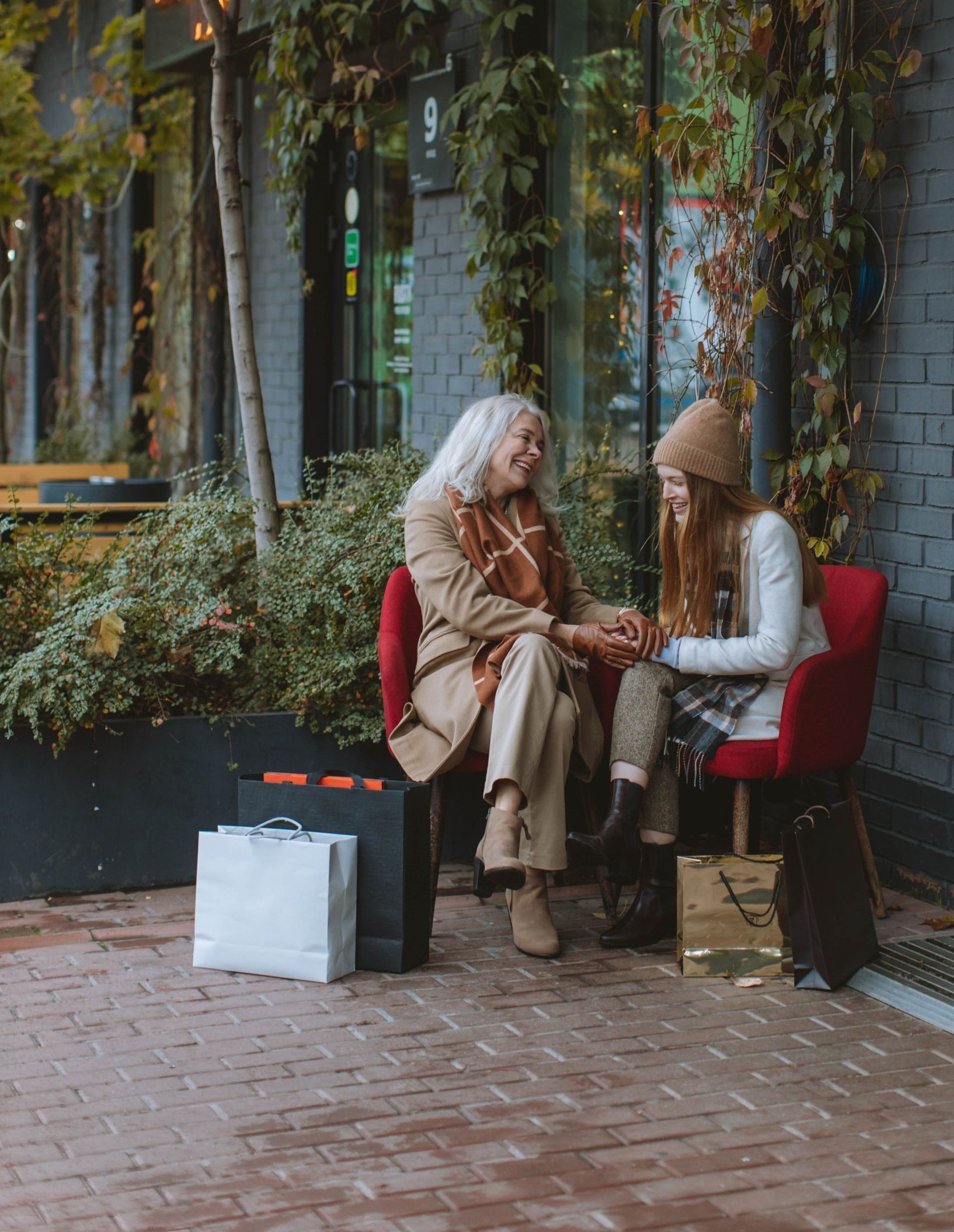 An elderly woman and a young girl are sitting on a bench holding hands.