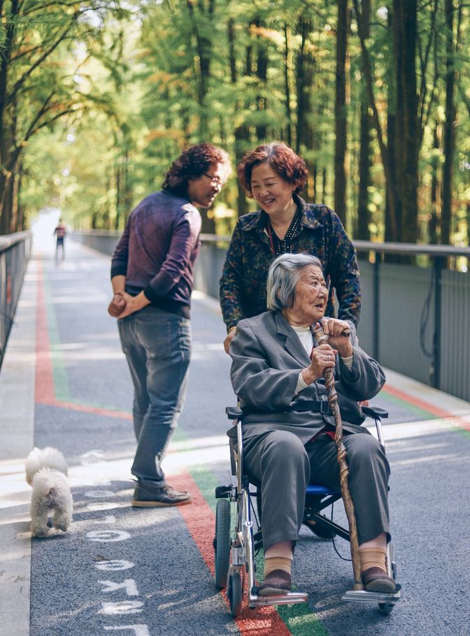 Older woman being pushed in a wheel chair through the park by her smiling daughter