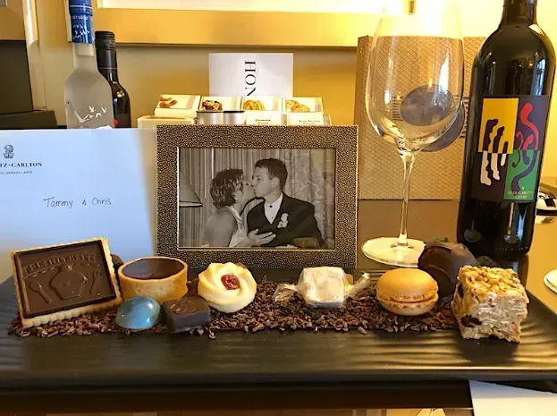 A display with sweets, wine, a framed photo of a couple kissing, and a welcome note.