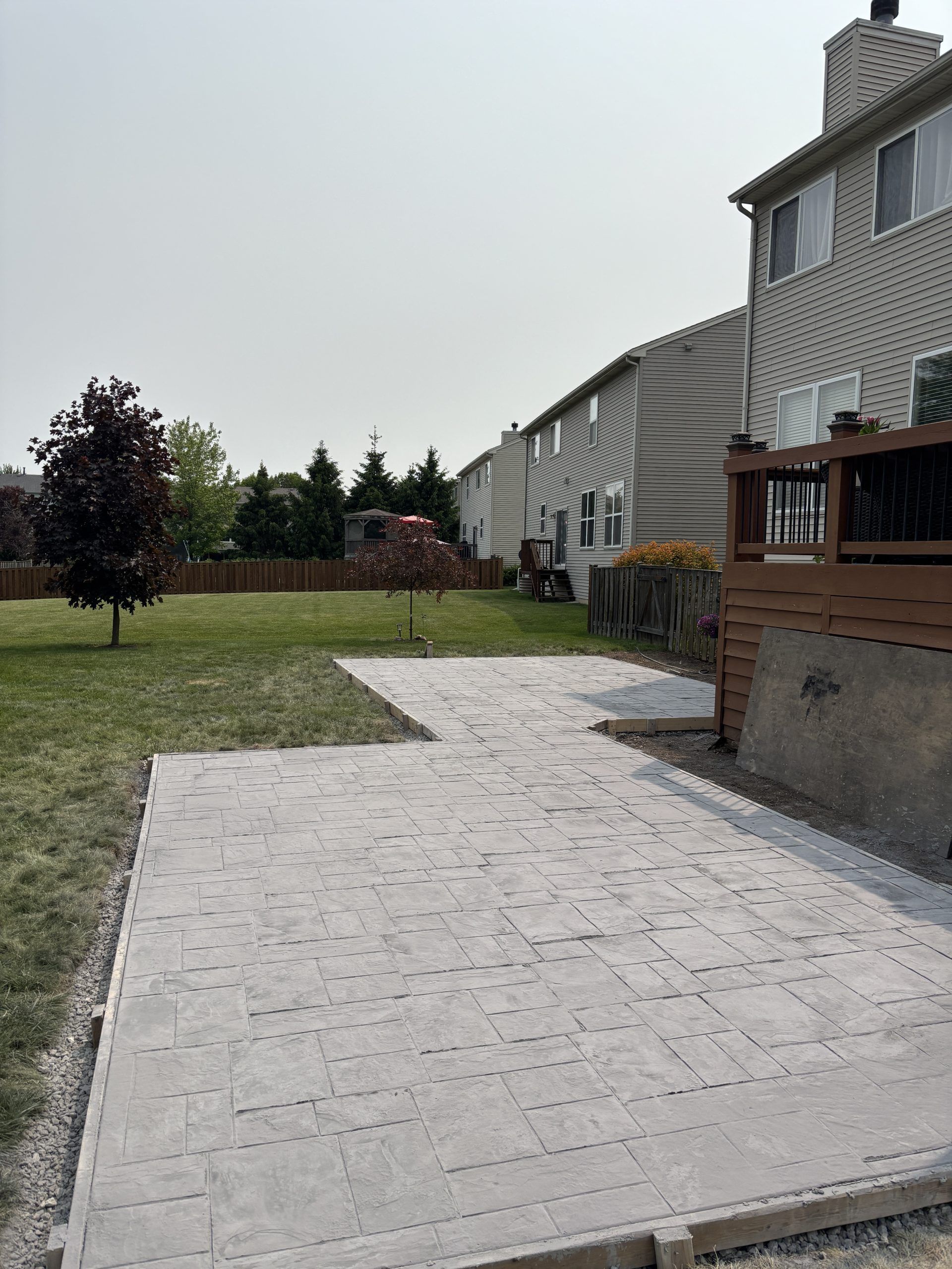 Backyard with a gray paved patio and lawn, townhouse buildings in the background.