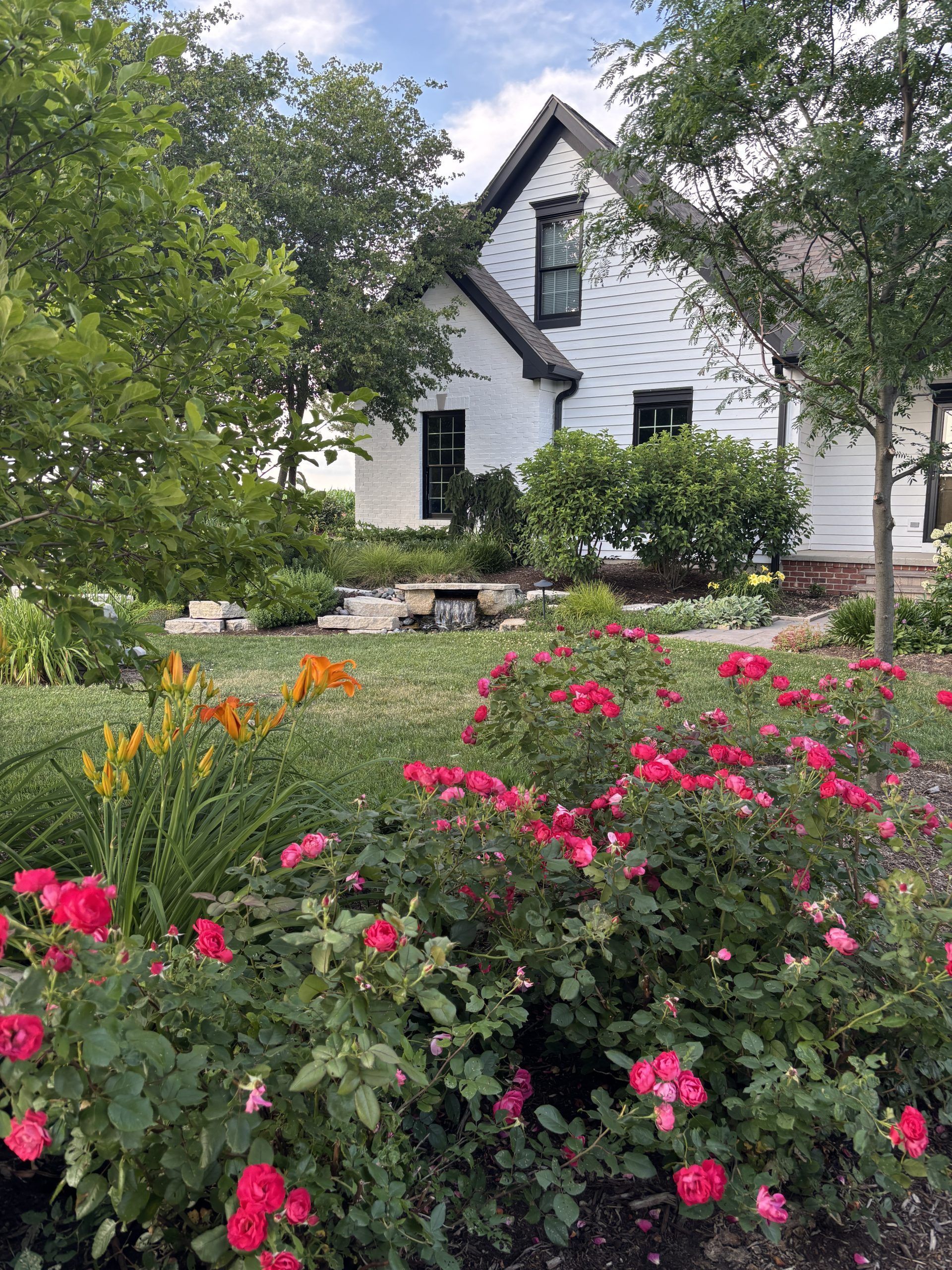 White house with black trim, surrounded by a lush garden of roses and greenery.