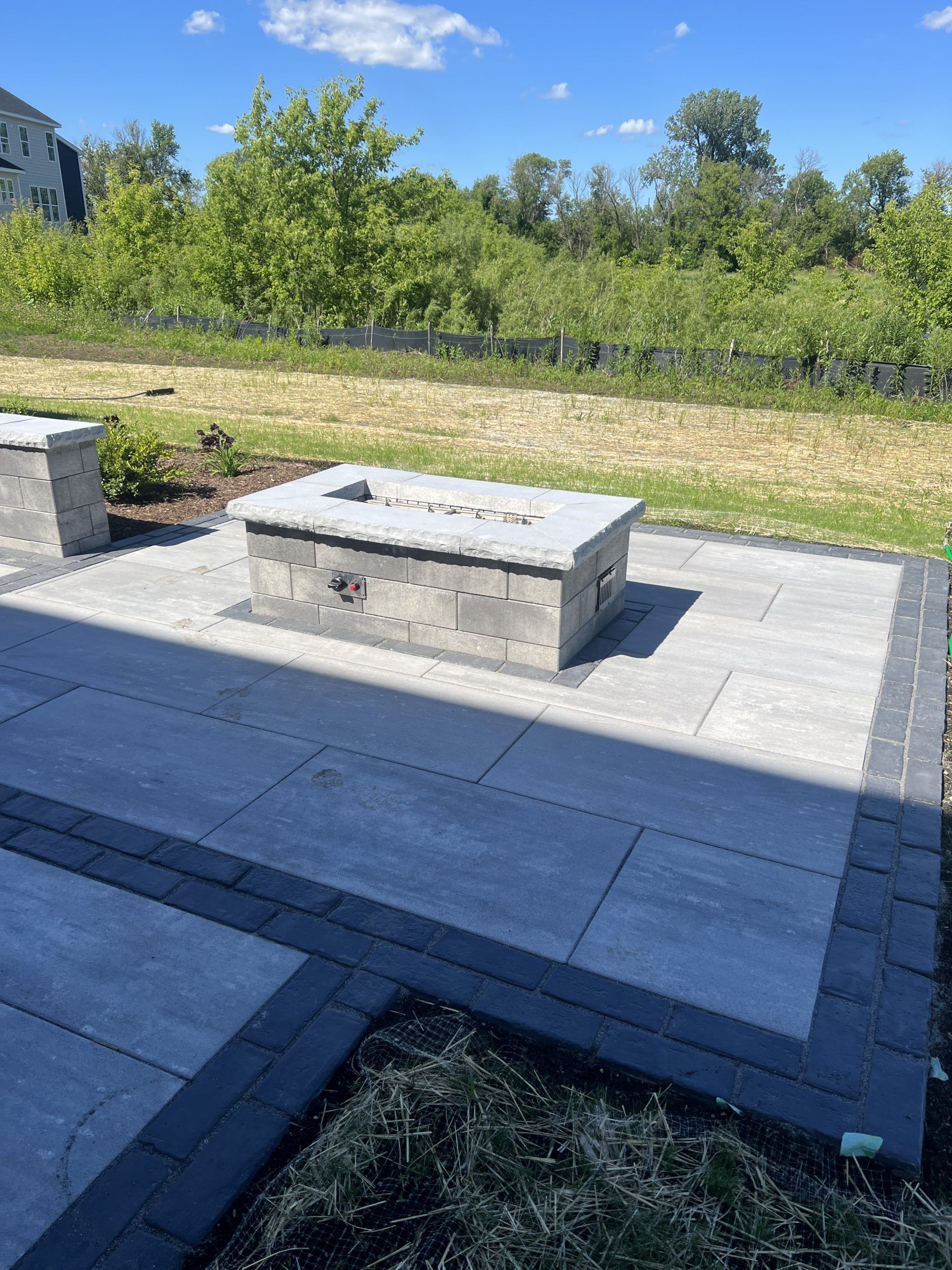 Concrete fire pit on a paved patio with surrounding landscaping, under a sunny sky.