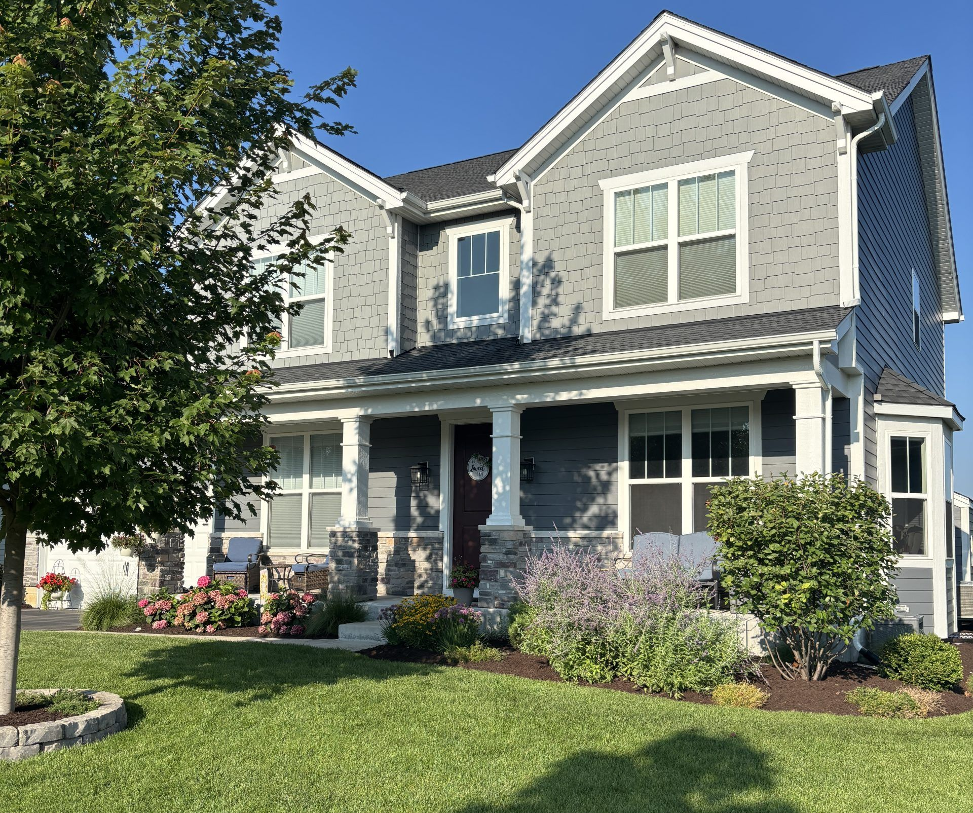 Two-story gray house with white trim, a porch, and a manicured lawn under a blue sky.
