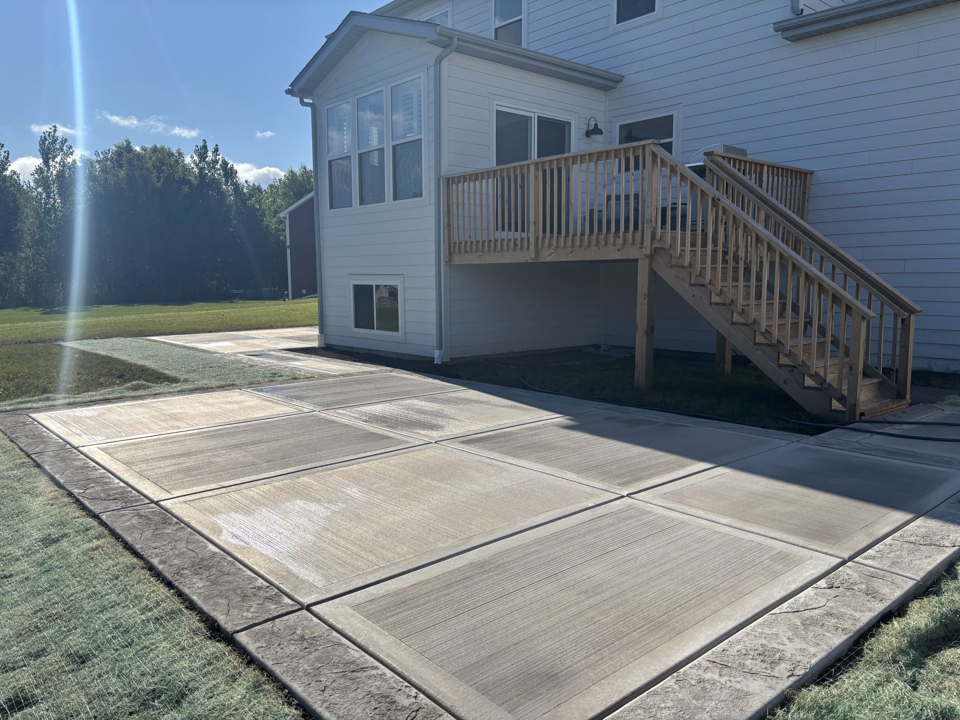 Backyard concrete patio with deck attached to a two-story house, sunny day.