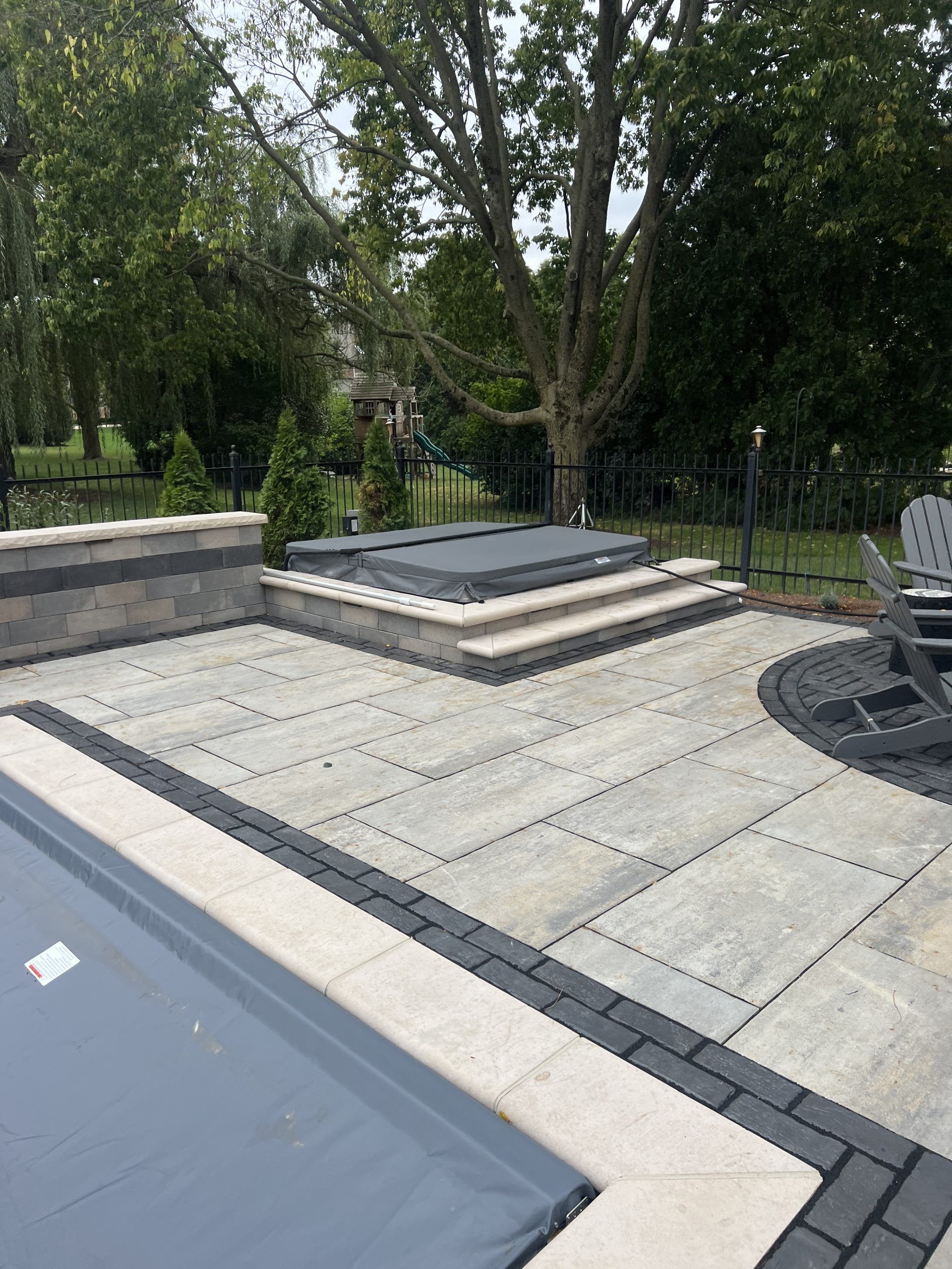 Stone patio with hot tub, steps, and pool in a backyard setting.