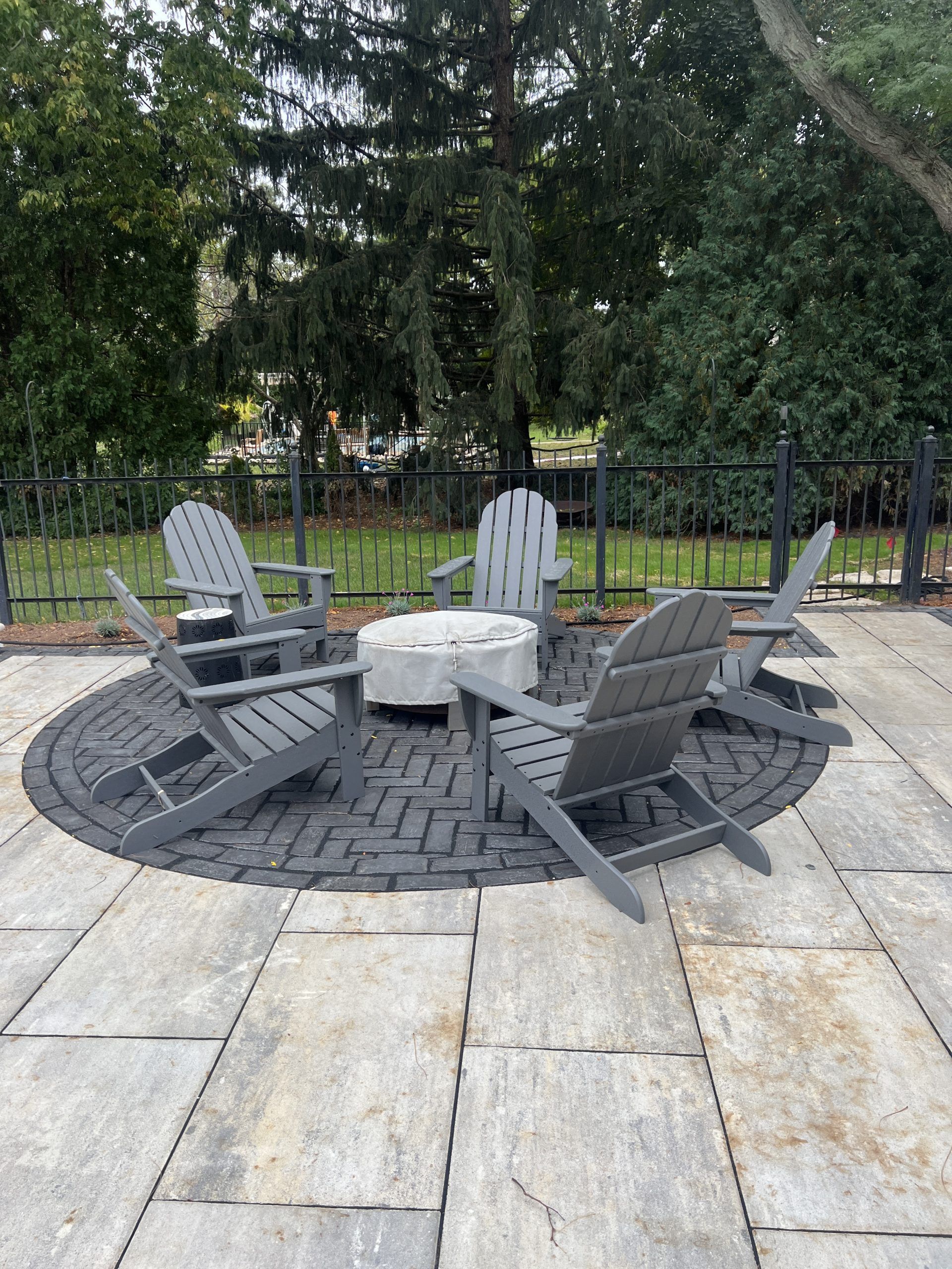 Outdoor seating area with gray Adirondack chairs arranged around a fire pit on a brick patio.