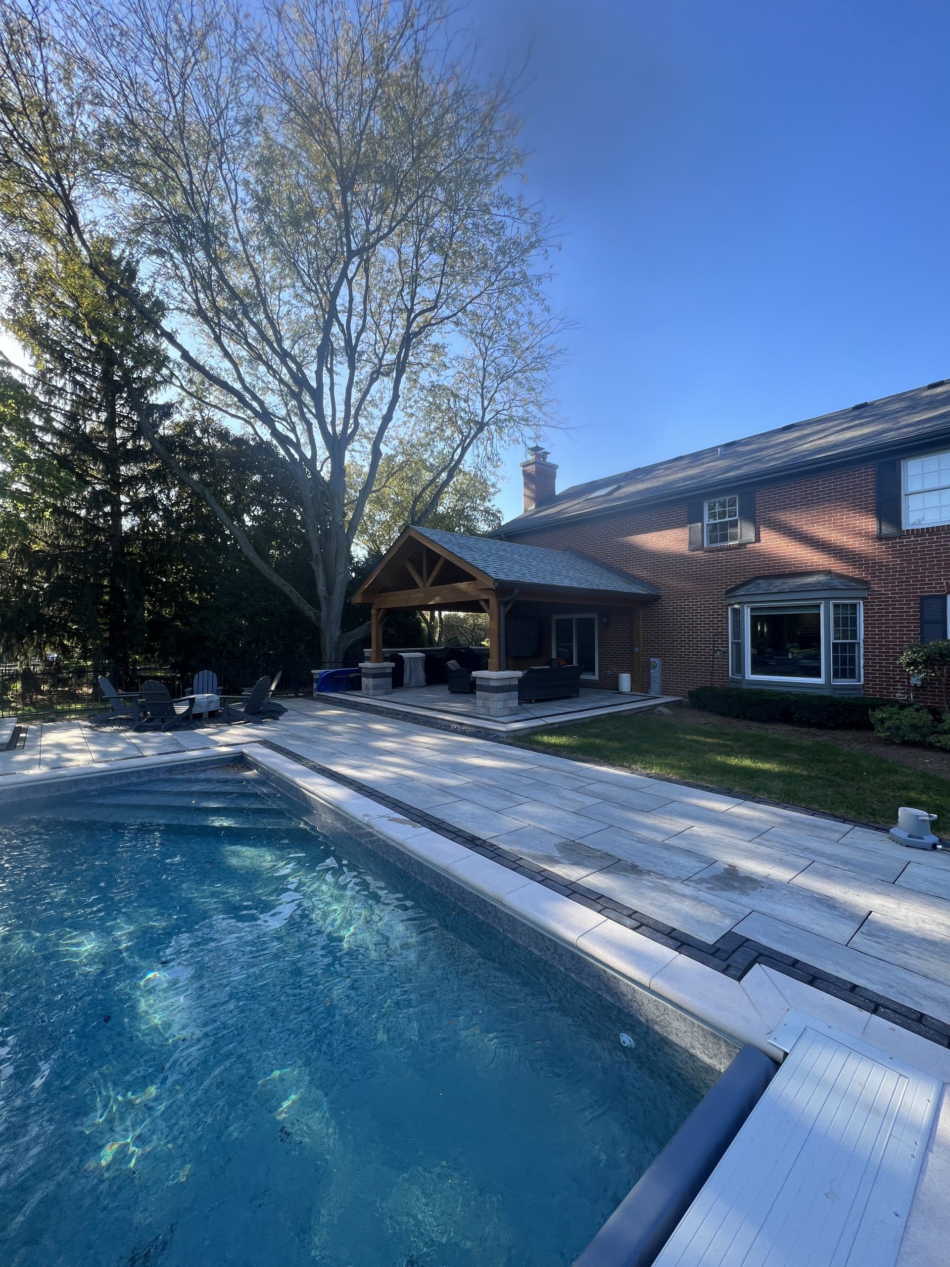 Poolside view of a brick house with a covered patio. A pool with clear water sits in the foreground.