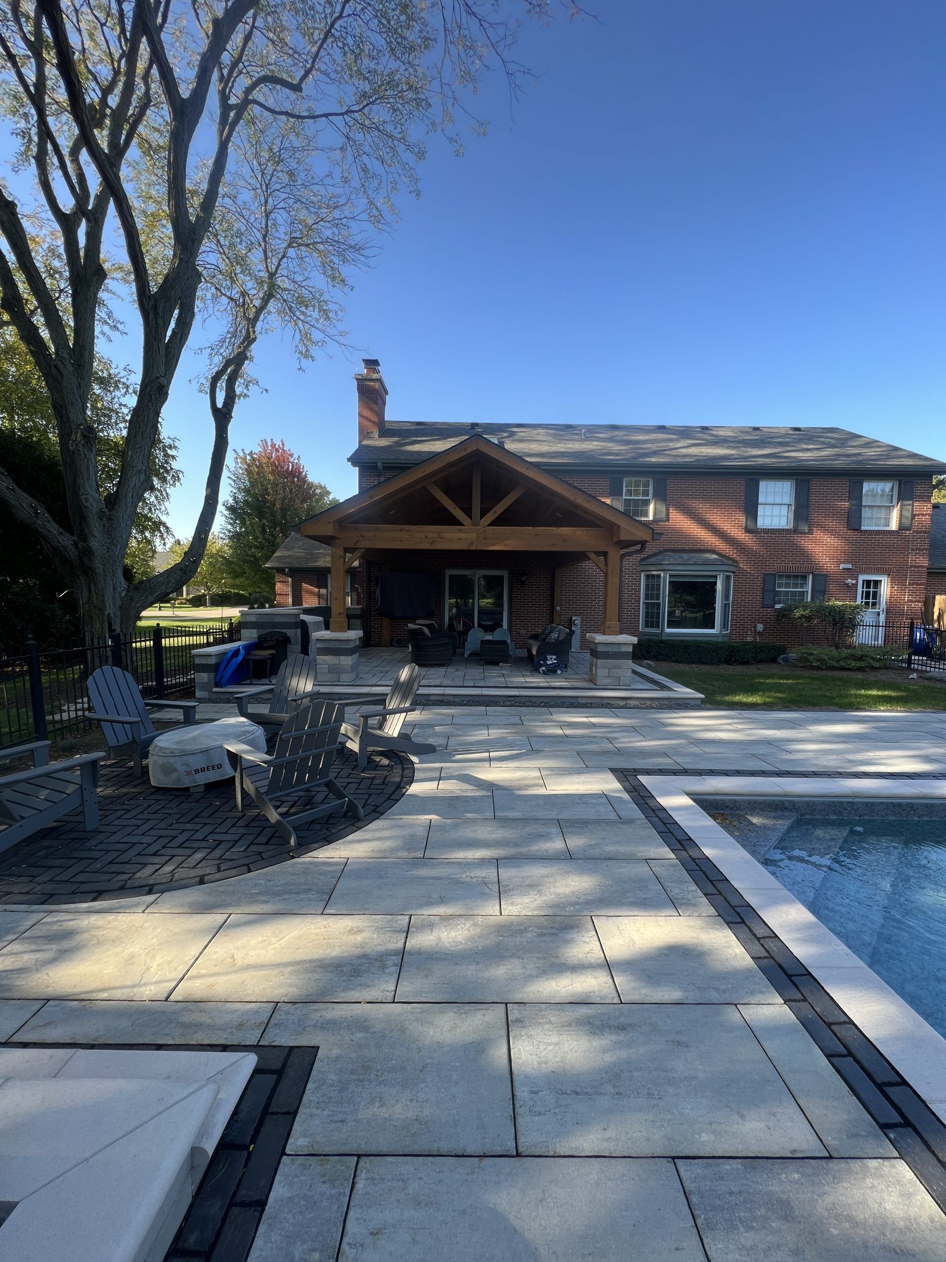 Backyard with pool, patio, and wooden pergola over a brick house. Blue sky overhead.