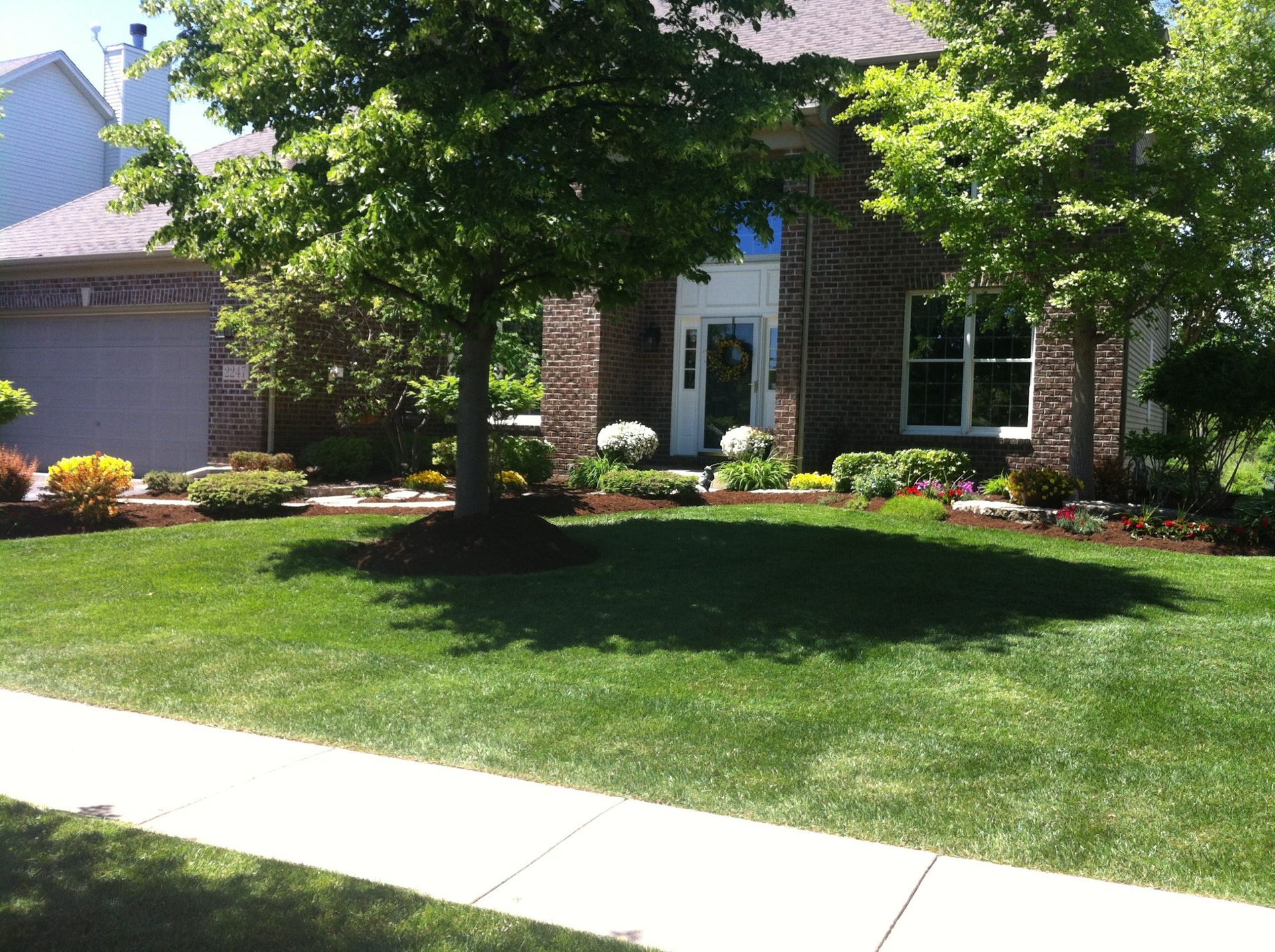 Well-kept house with brick exterior, manicured lawn, and trees casting shadows.