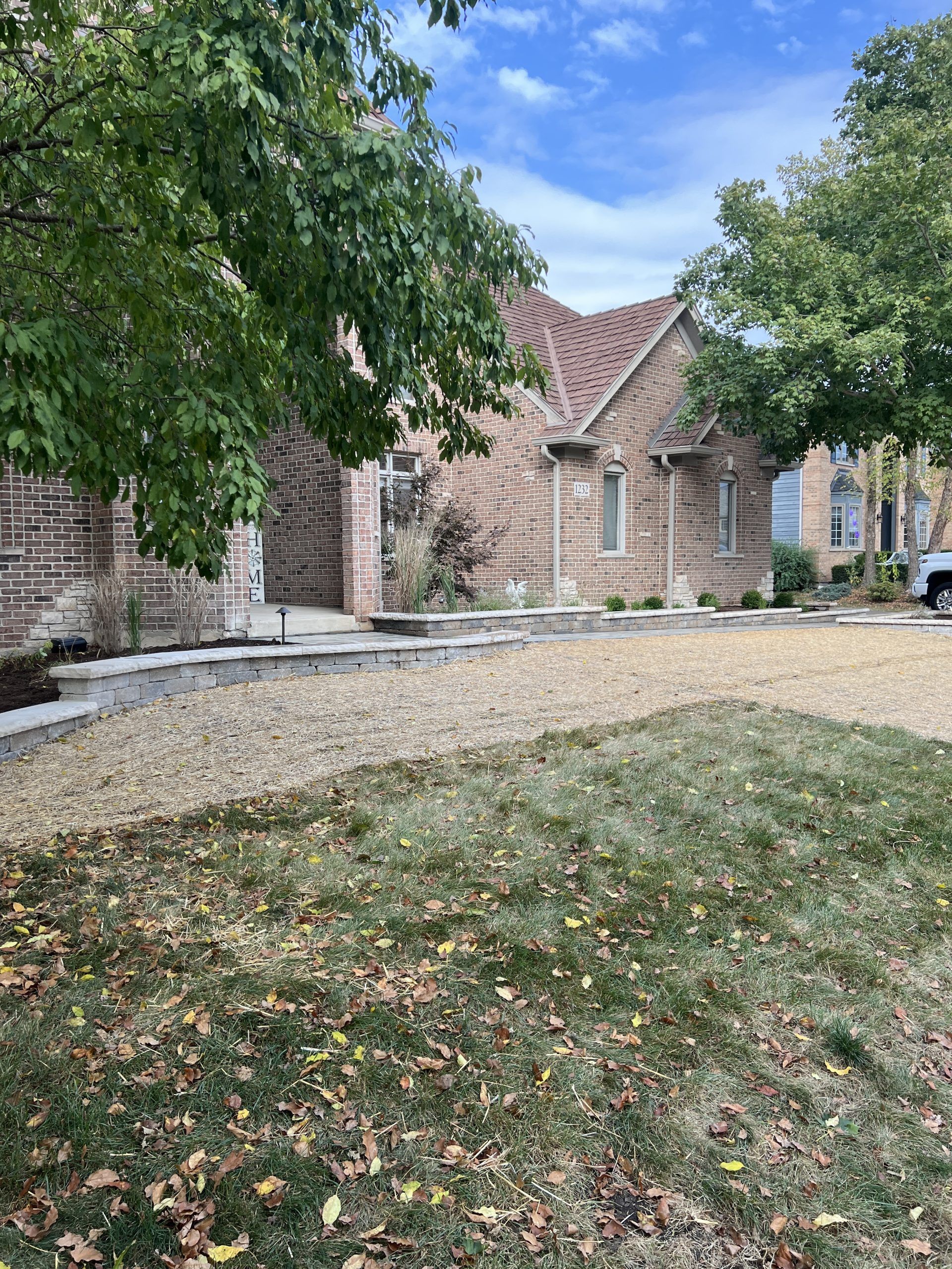 Brick building with a red-tiled roof, flanked by trees and a dry lawn. Cloudy sky in the background.