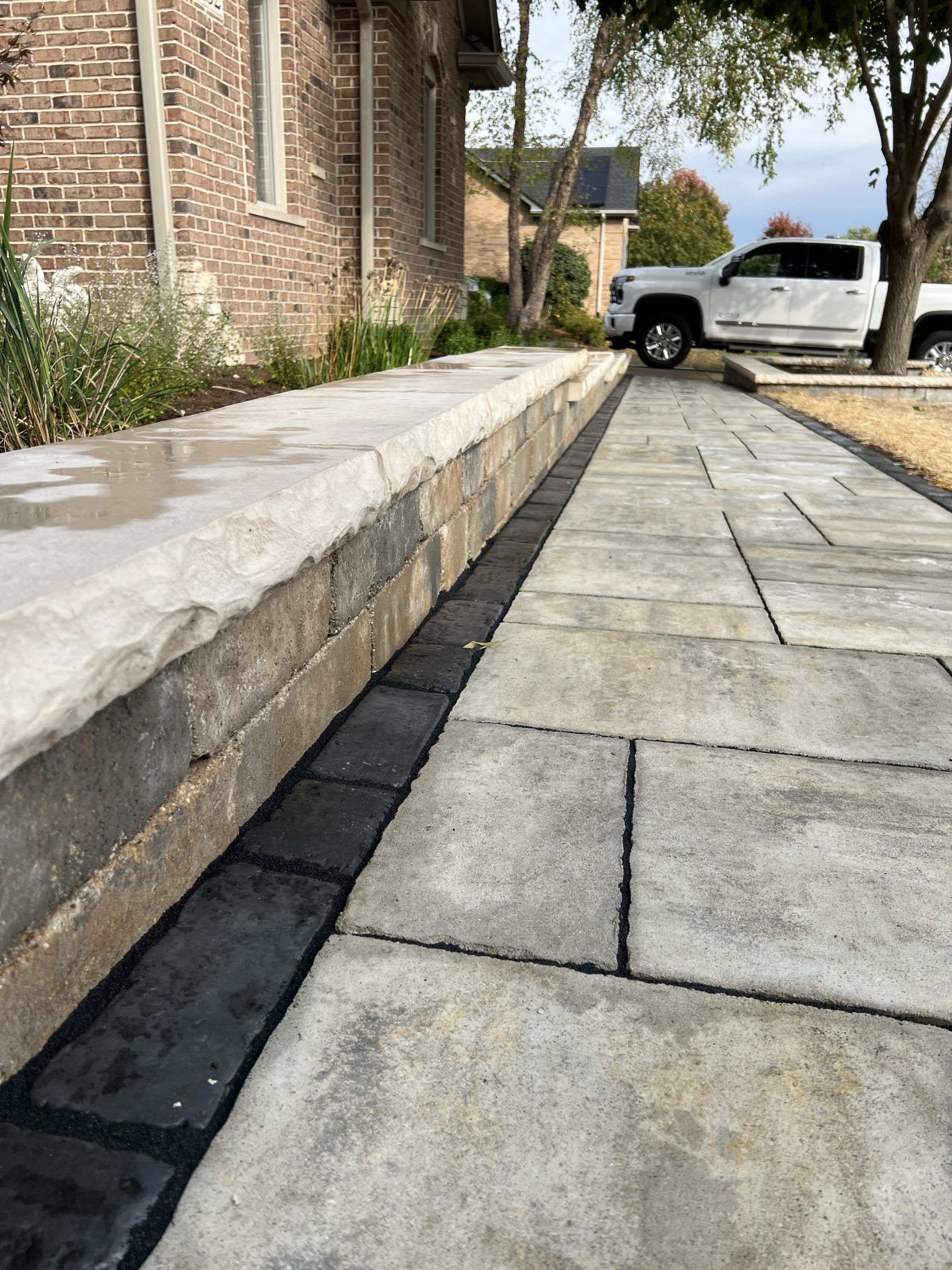 Stone walkway next to a low retaining wall; brick building on the left, truck in the background.