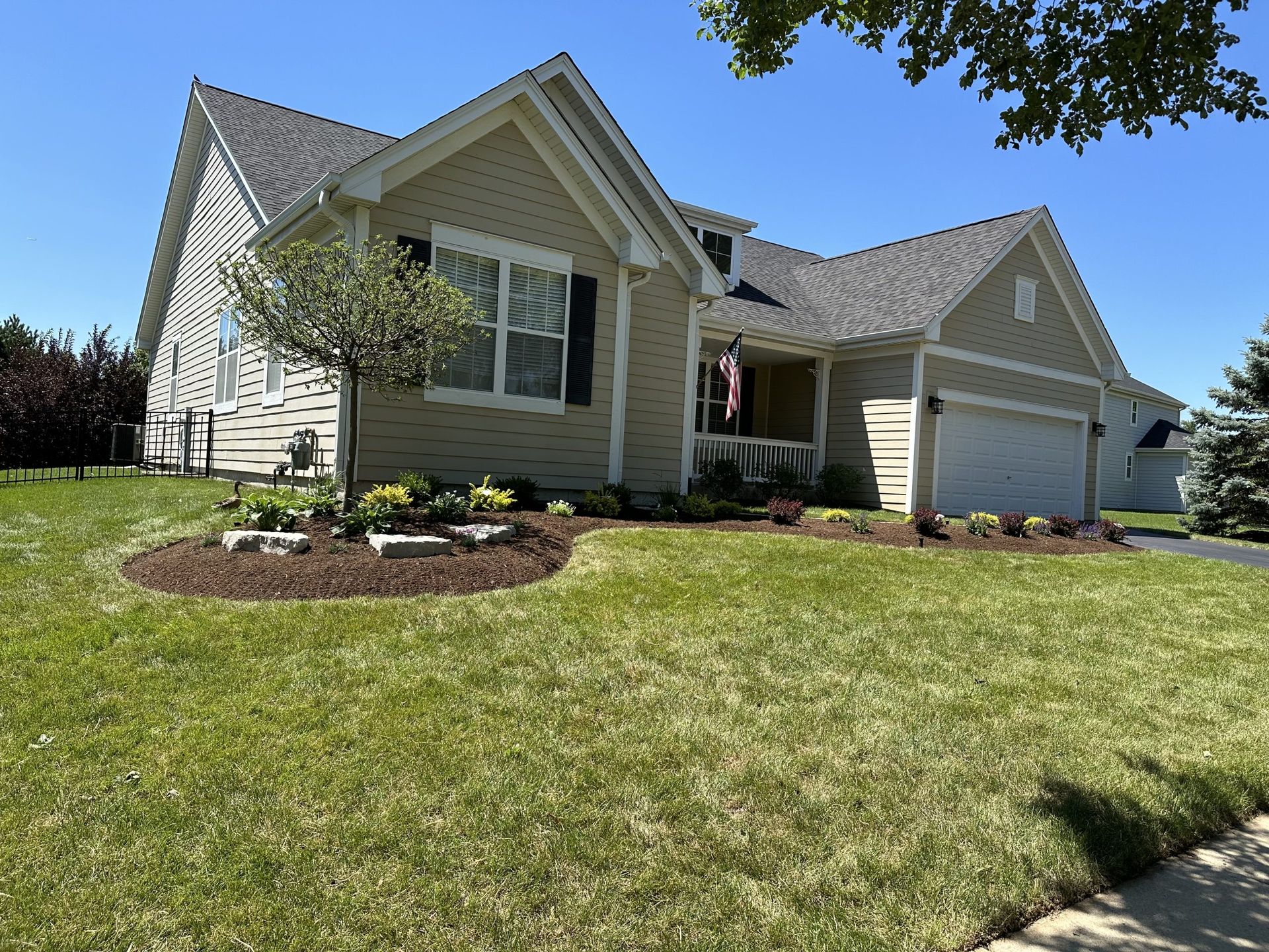Beige house with a well-manicured lawn and landscaping on a sunny day.