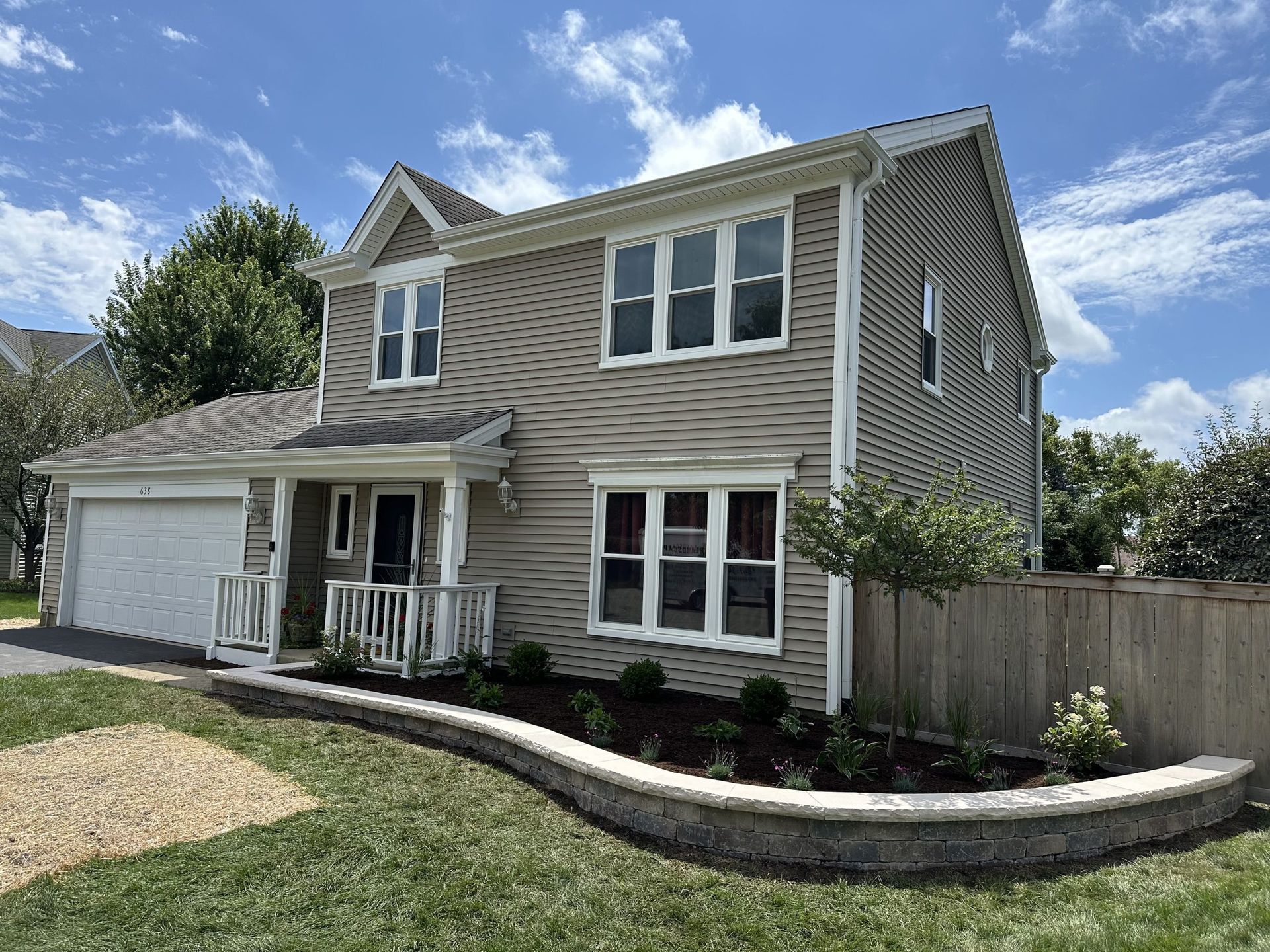 Two-story house with beige siding, white trim, and a small front garden with a curved retaining wall.
