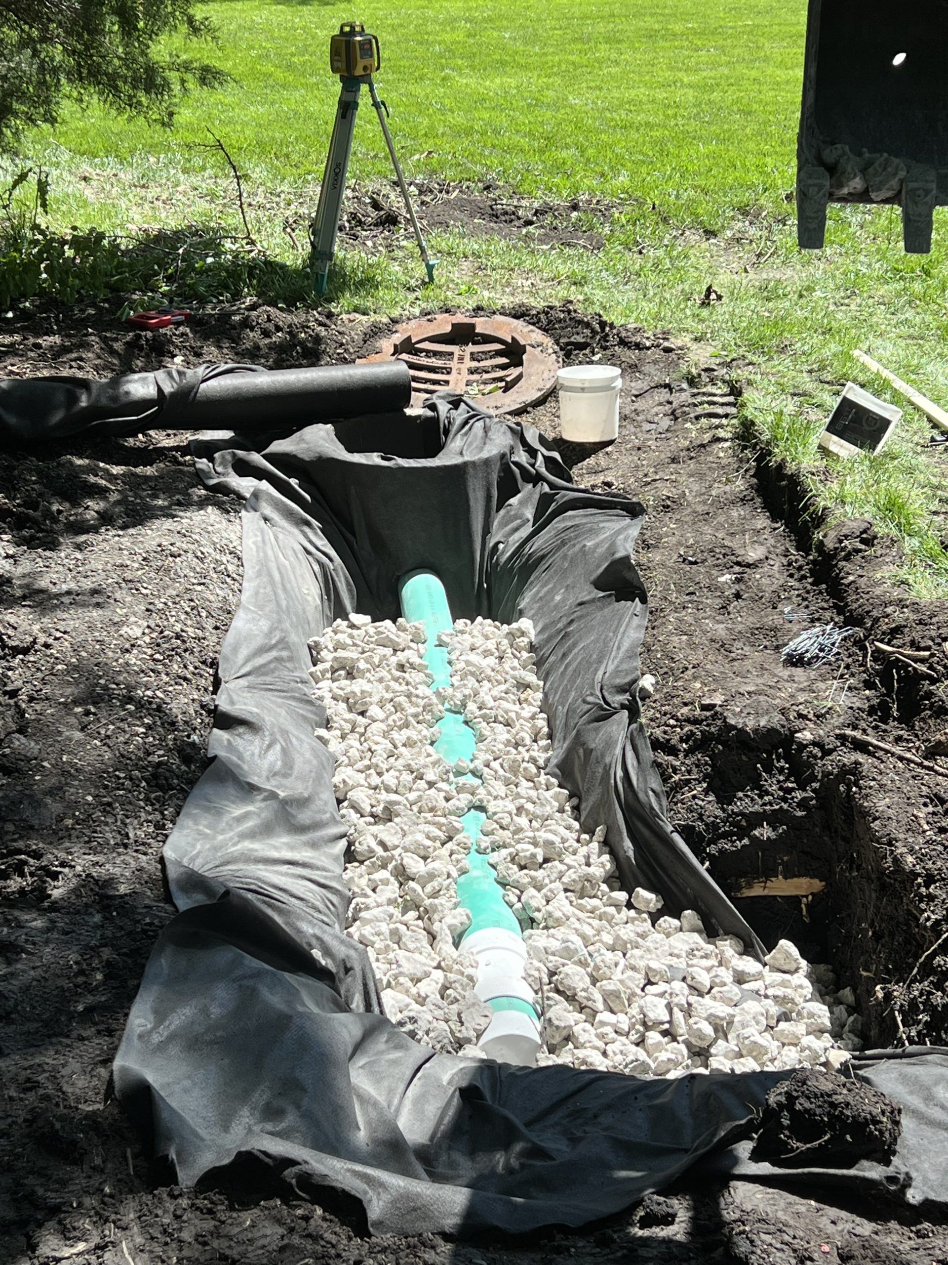 Drainage system installation in a trench, with gravel, pipe, and black fabric, outdoors.