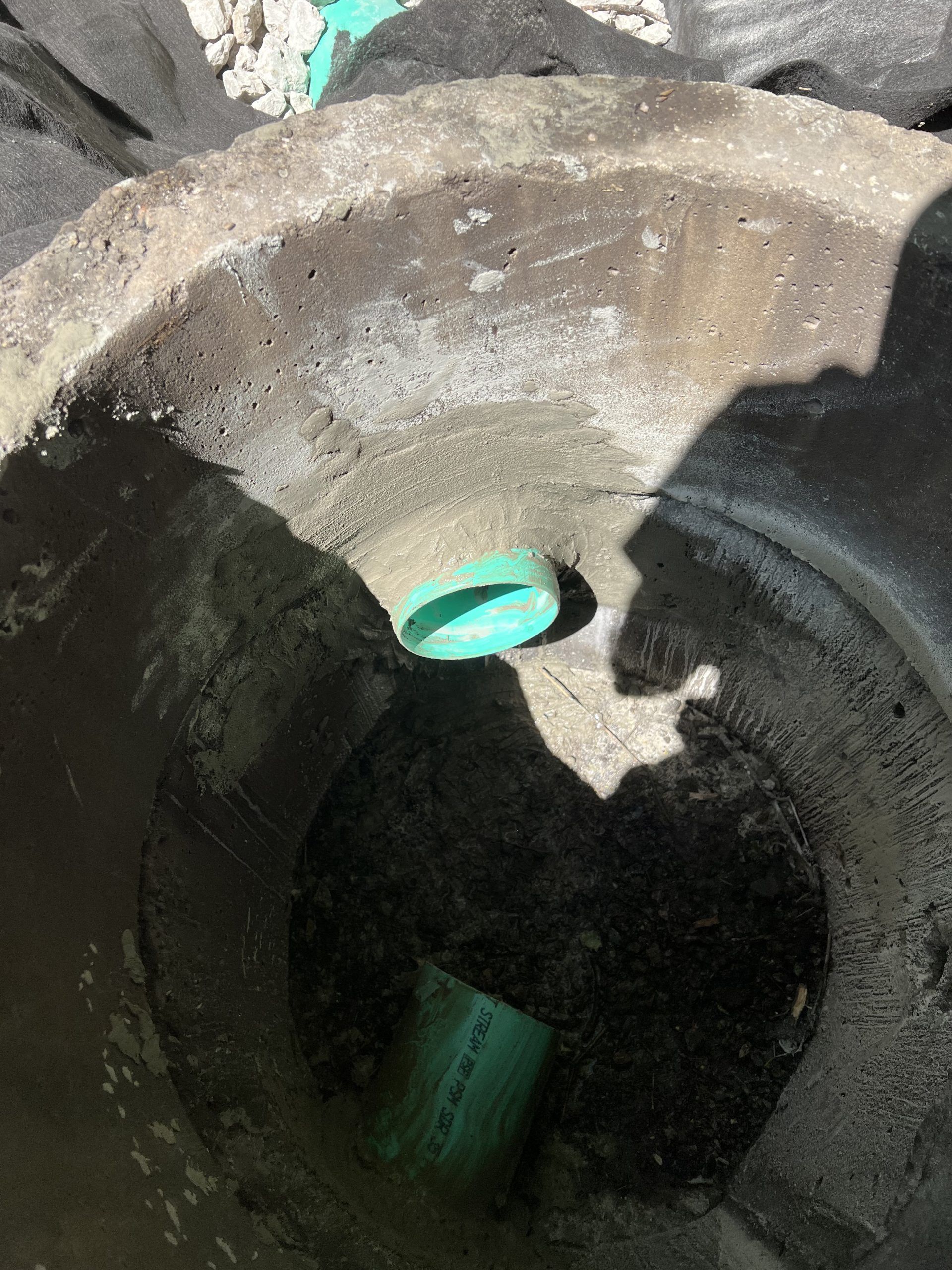 Looking down into a concrete manhole. Two green pipes are visible.