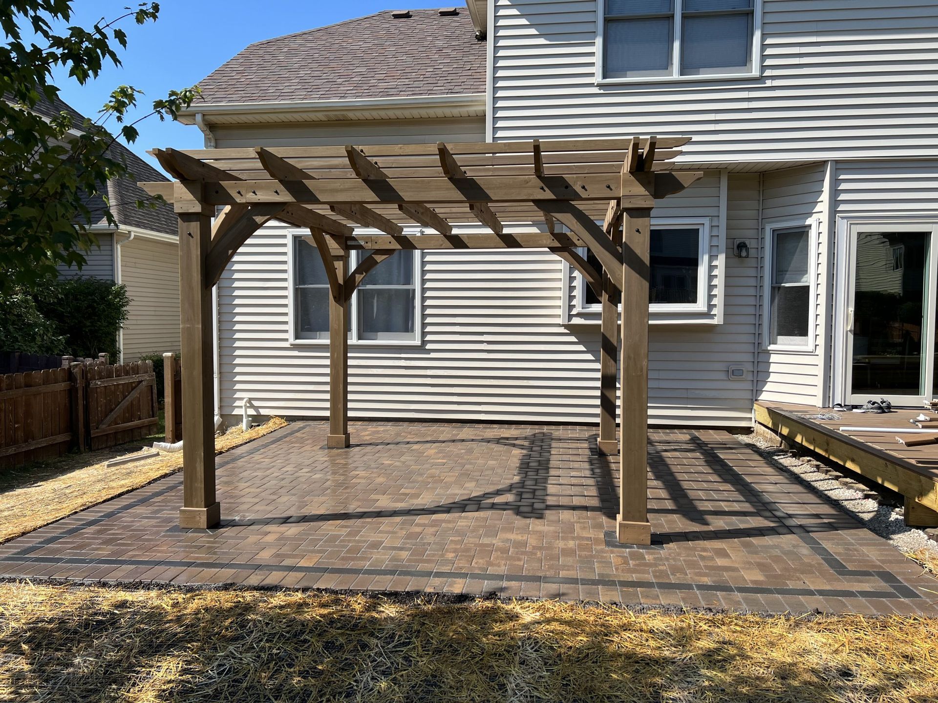 Pergola on a paved patio in front of a house.
