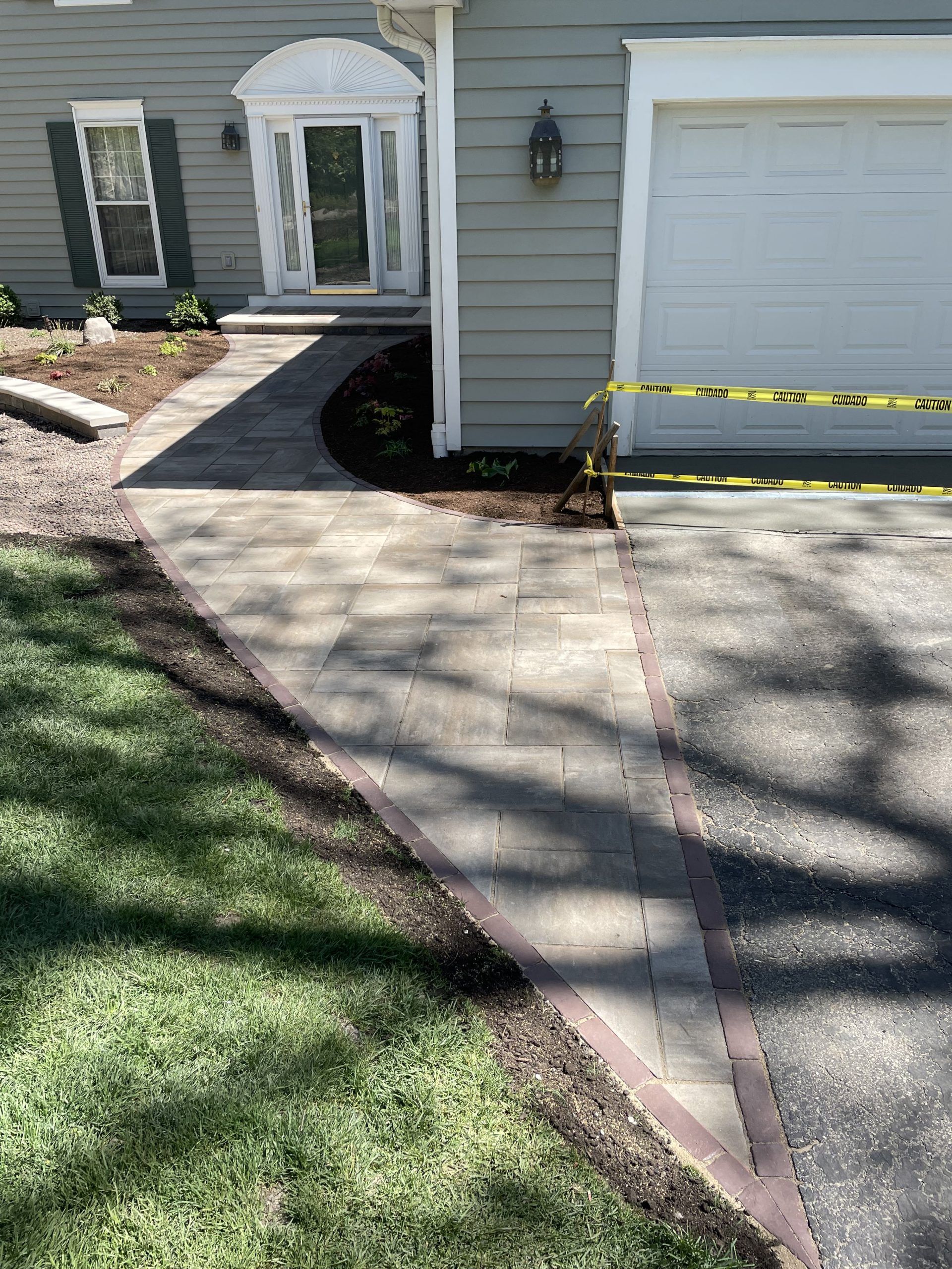 Newly constructed paved walkway with a brick border leading to a house entrance and garage.