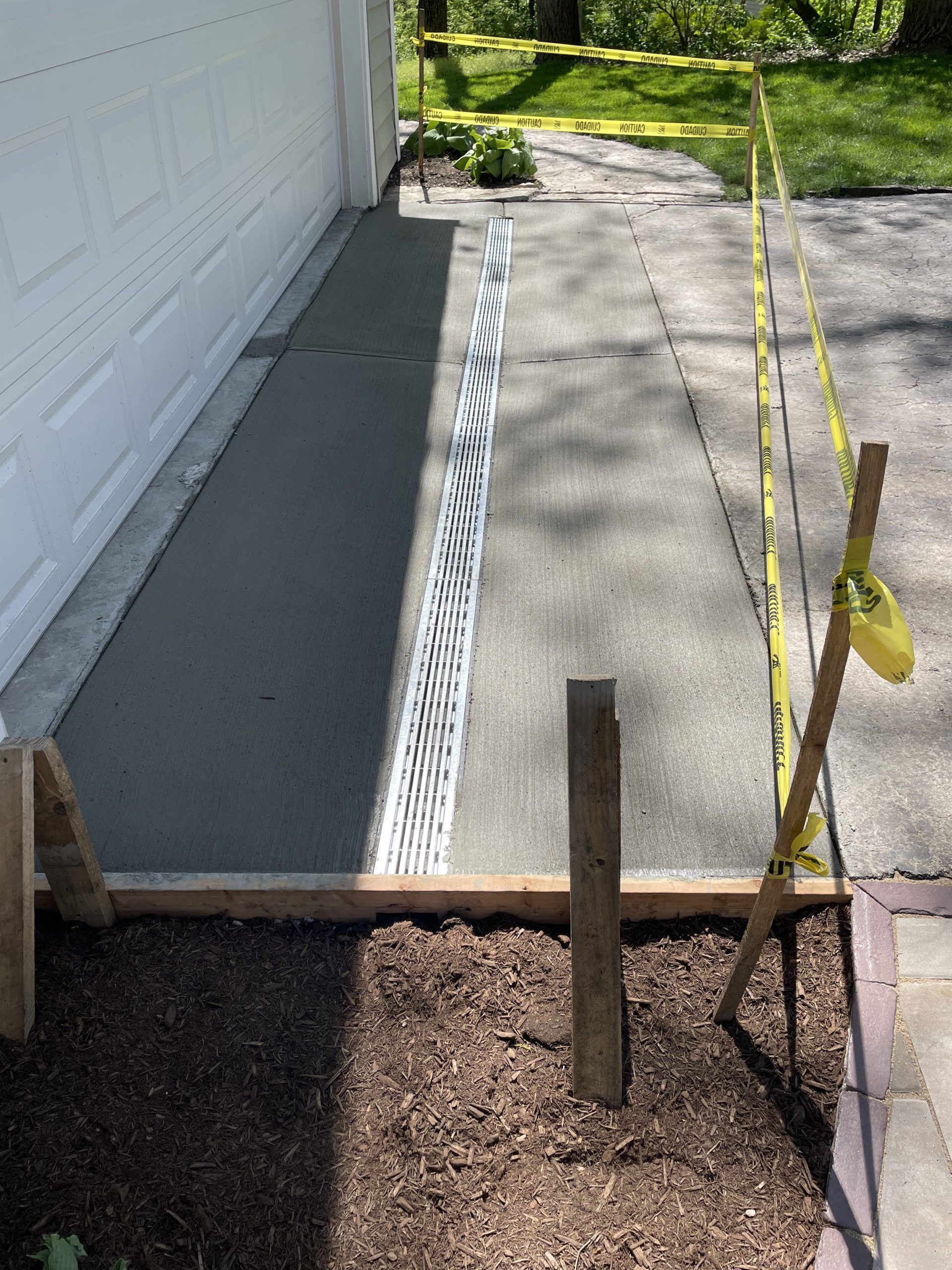 Freshly poured concrete walkway next to a garage, marked with caution tape and stakes.
