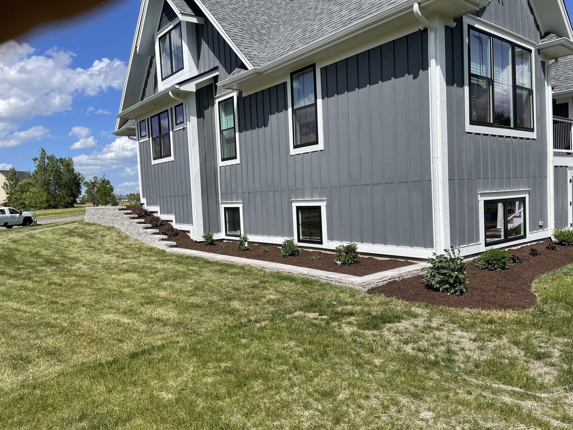 Gray house with white trim, landscaping, and a grassy yard under a blue sky.