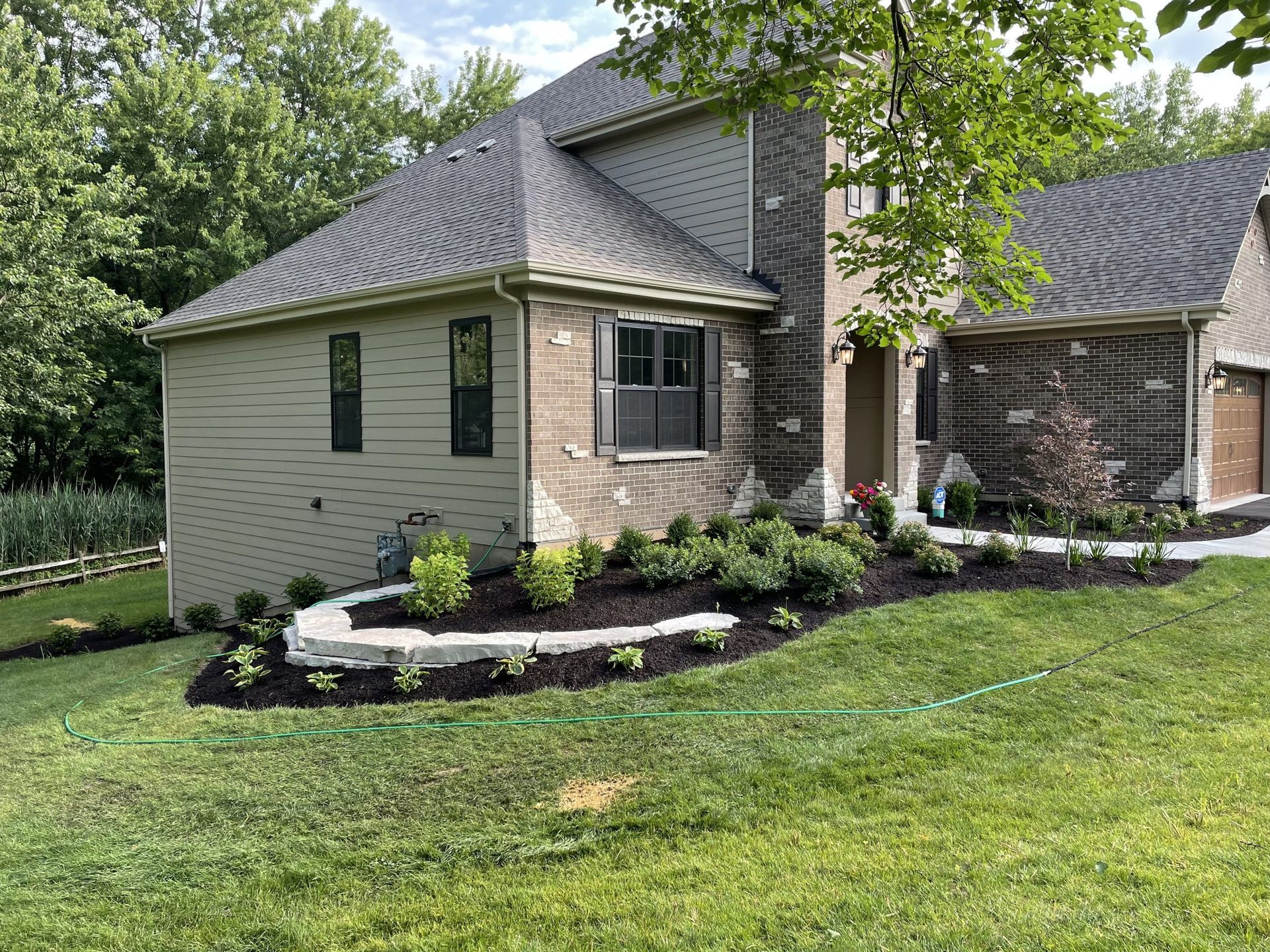 House exterior with landscaping and dark roof. Green lawn and trees in background.