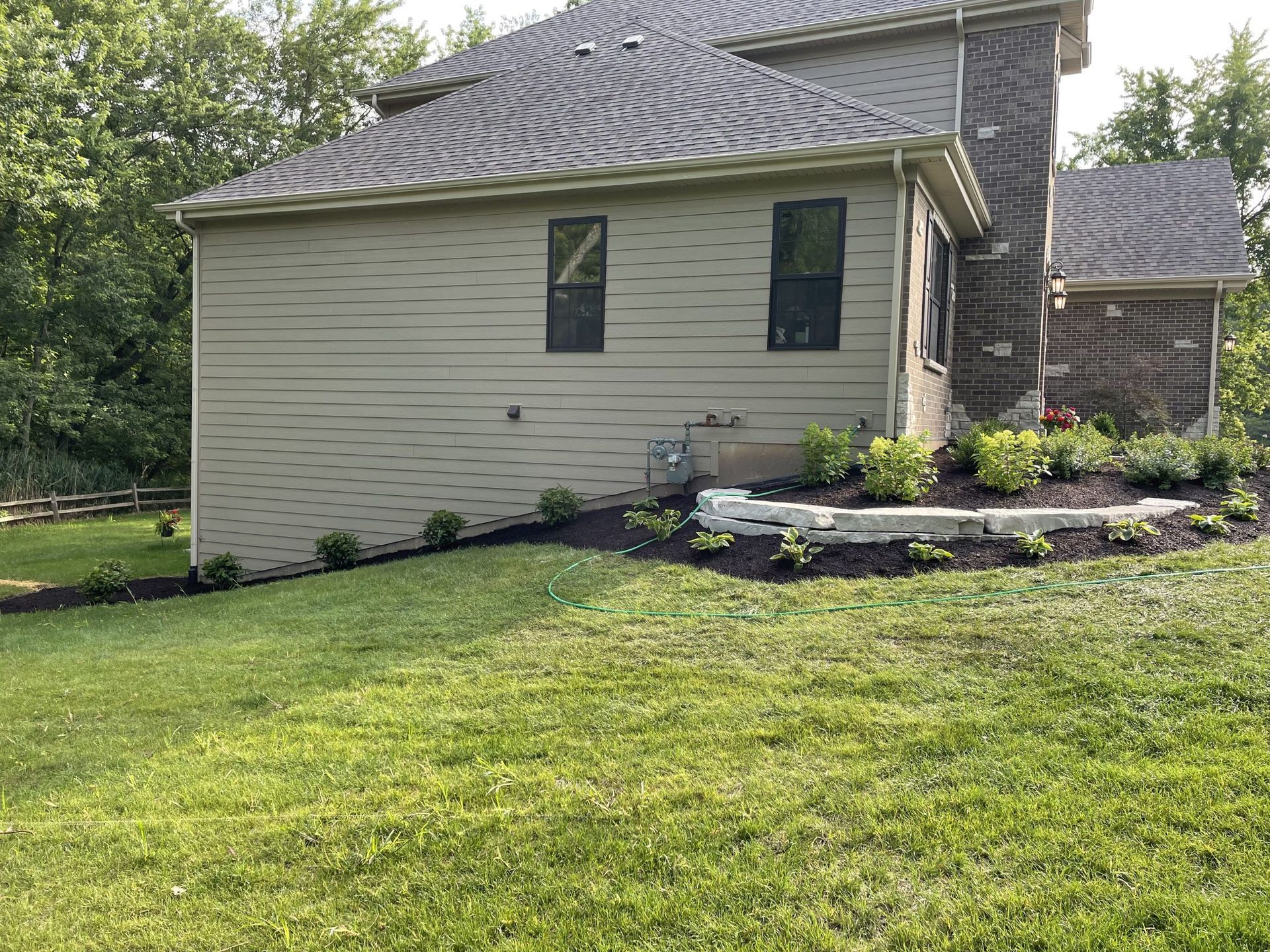 House exterior with tan siding and a stone chimney, surrounded by green grass and landscaping.