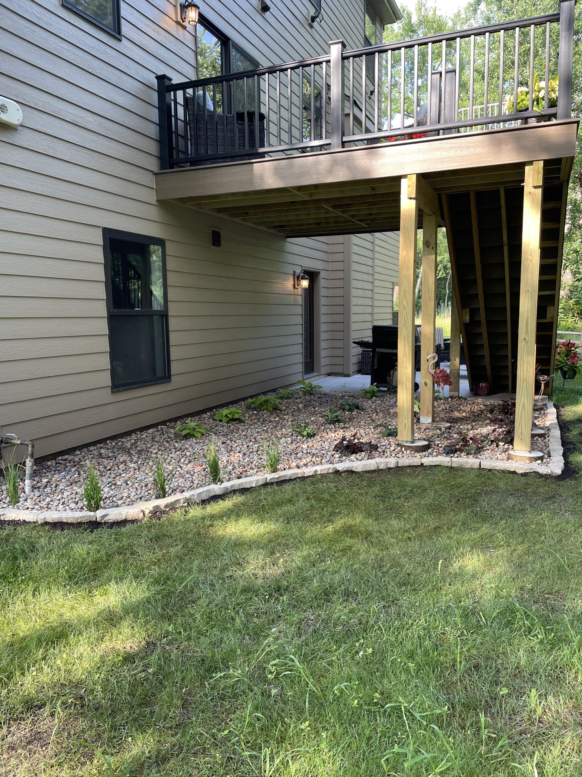 Beige house with a second-story deck over a lower level with a stone-edged garden and steps.