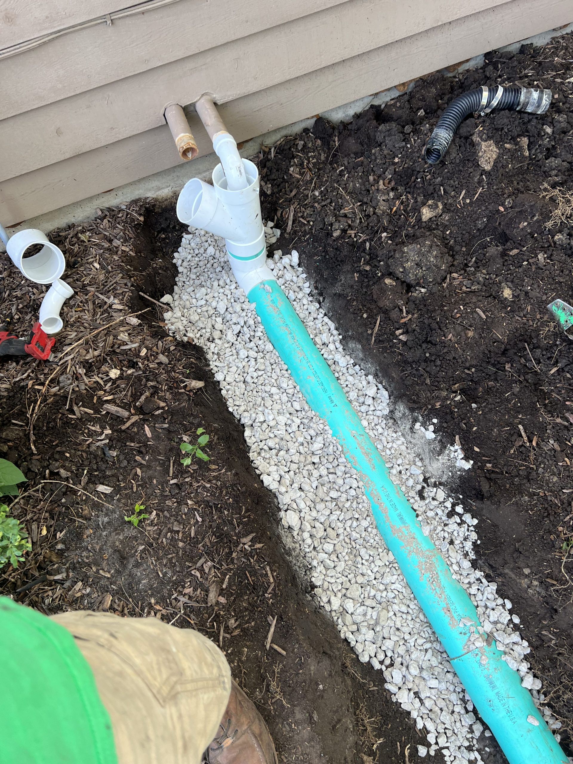 A blue pipe in a trench filled with gravel, next to a building. Plumbing work is in progress.