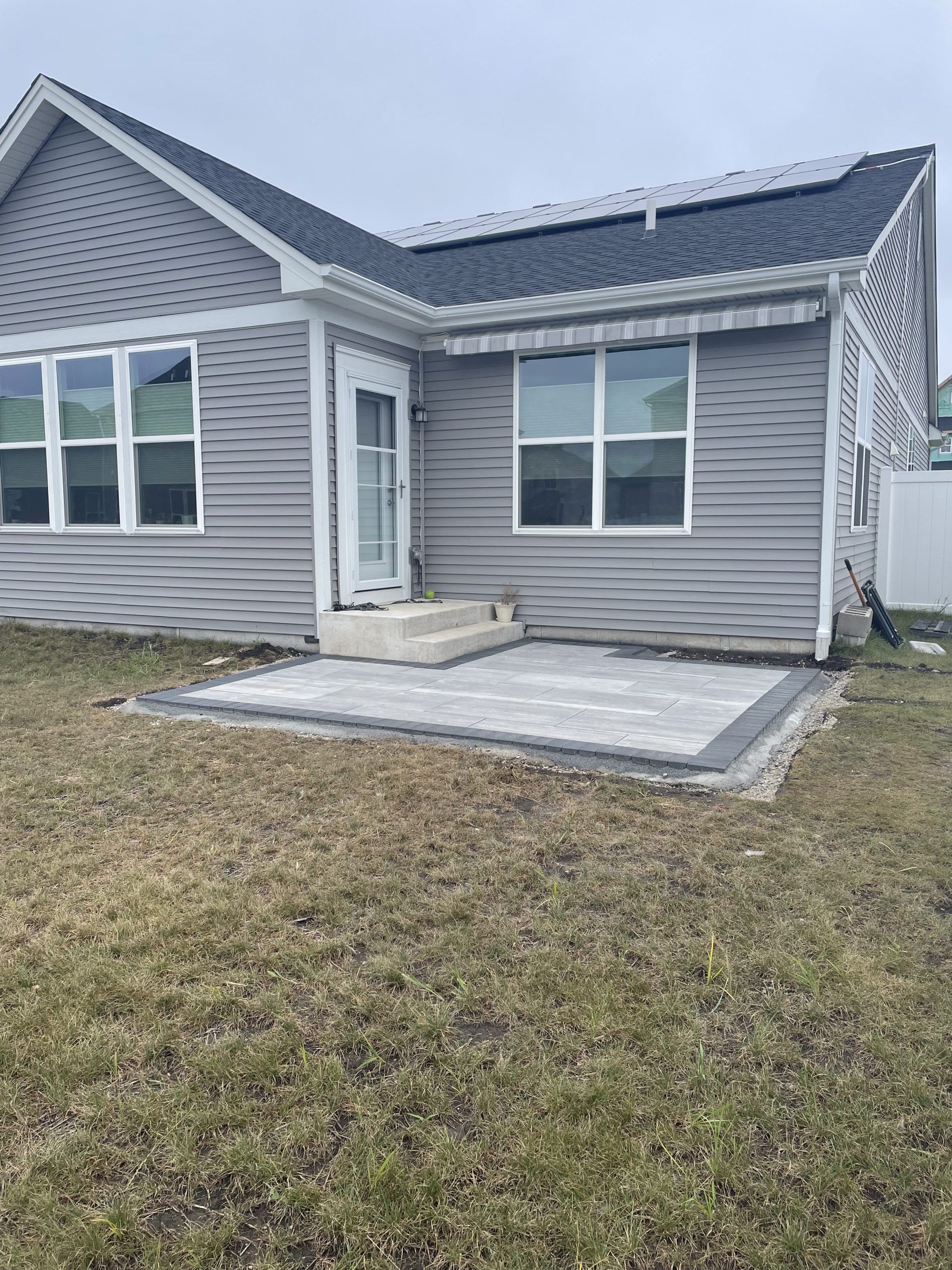 Patio with gray pavers, next to a house with gray siding.