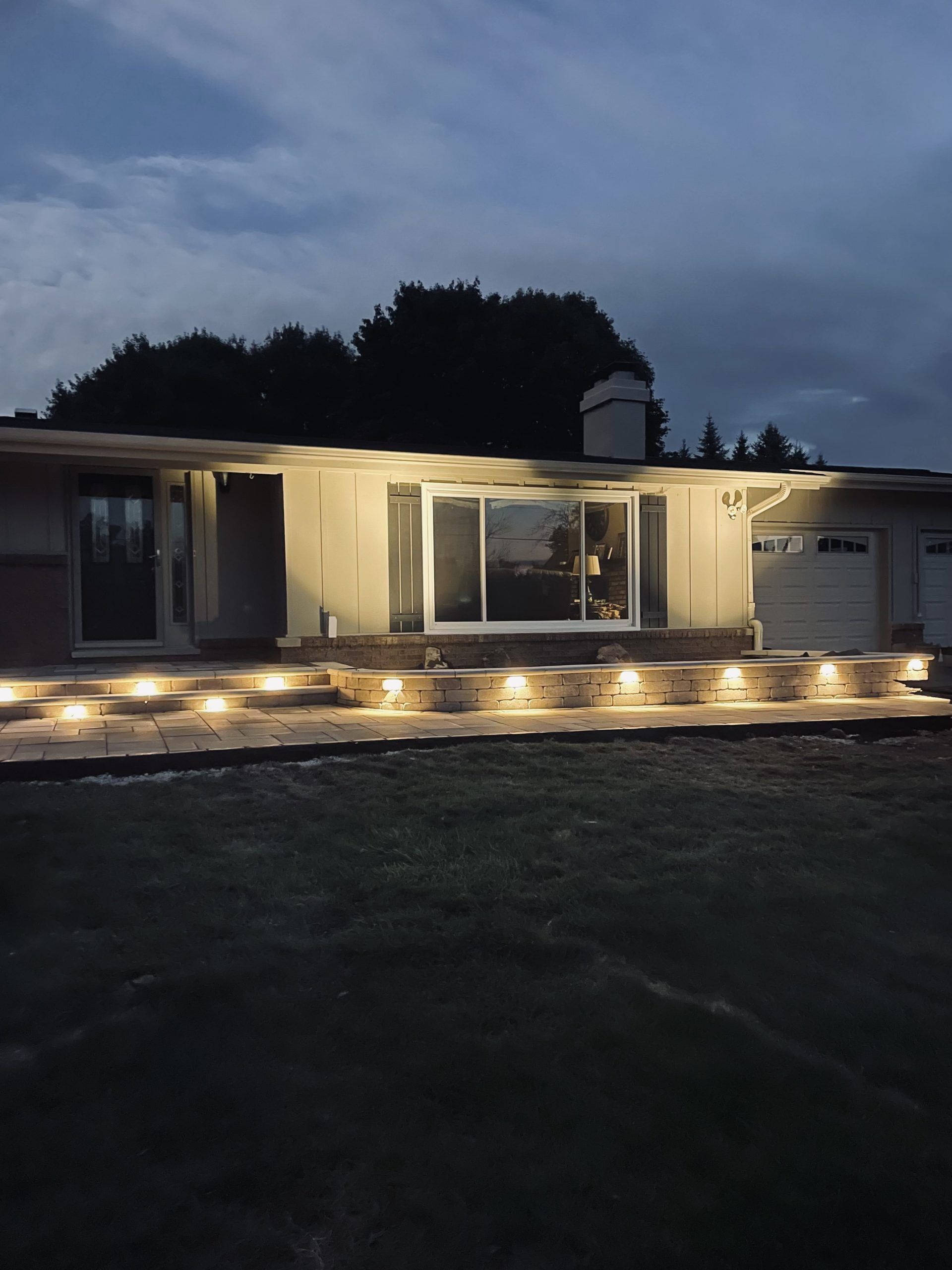 House exterior at dusk, illuminated pathway leading to entrance with lit steps and overhead lights.