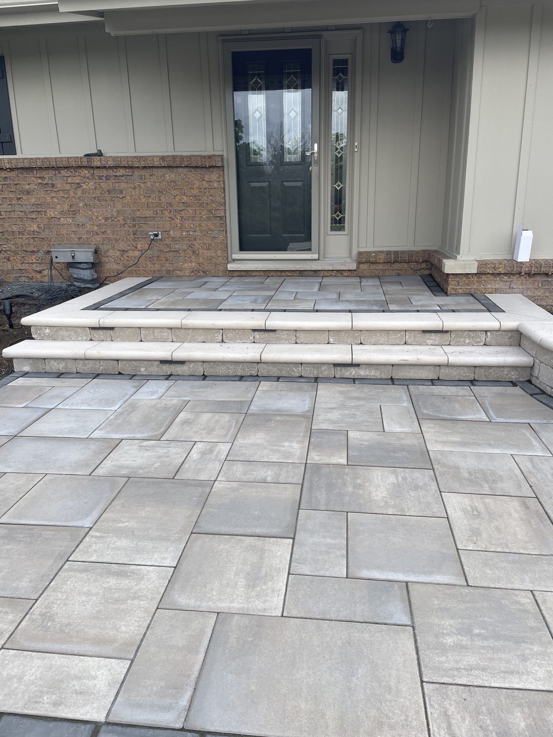 Stone patio with steps leading to a front door with glass panels.