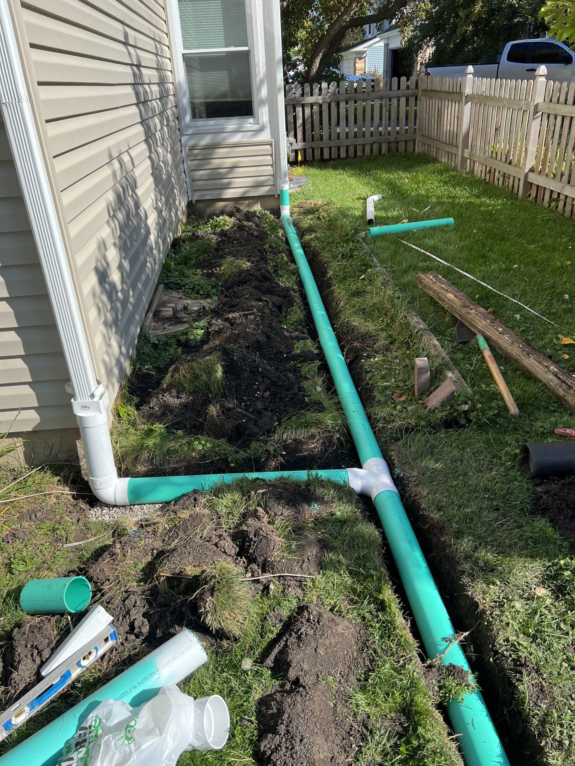 Green drainage pipes being installed next to a house with a white downspout.