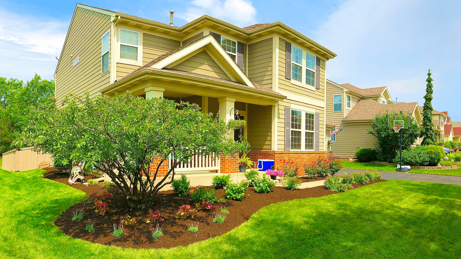 Two-story beige house with a porch and landscaped front yard; sunny day.
