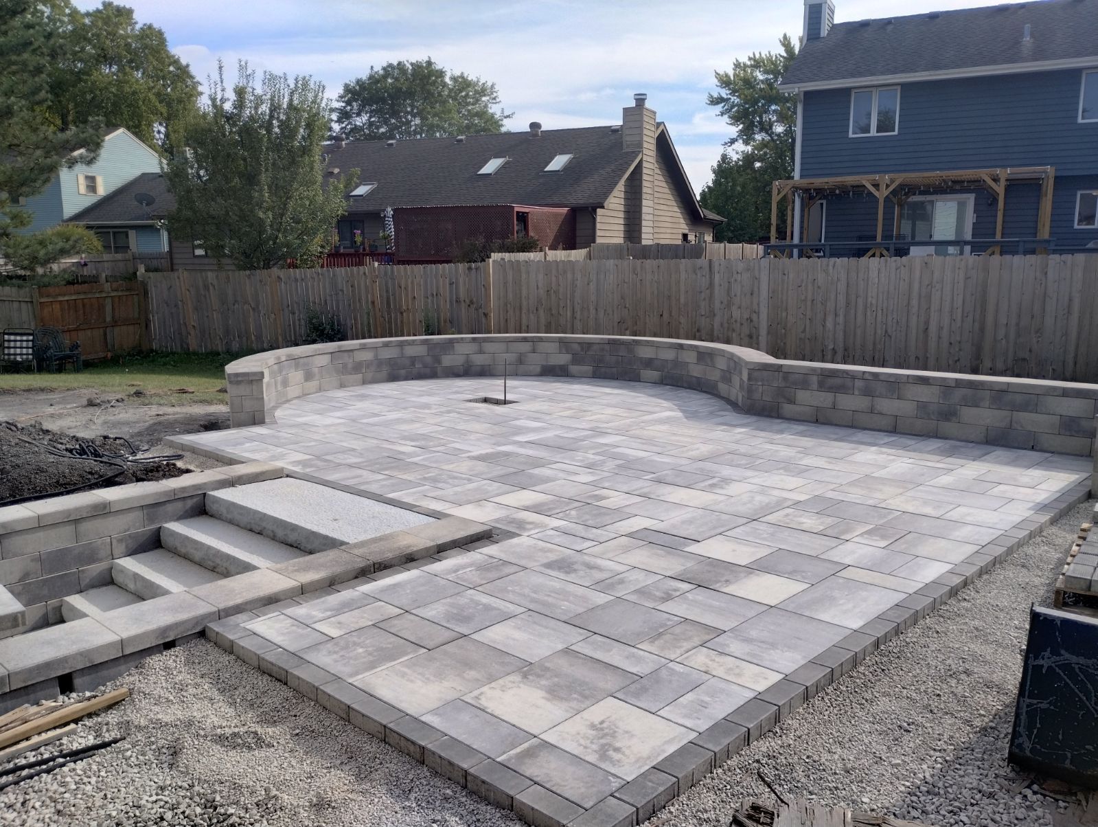 Stone patio with retaining wall, steps, and gray pavers. Backyard setting.