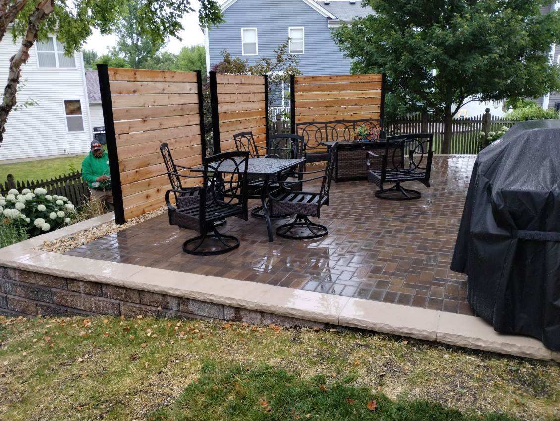 Patio with black furniture, wooden screen, brick border, and covered grill.
