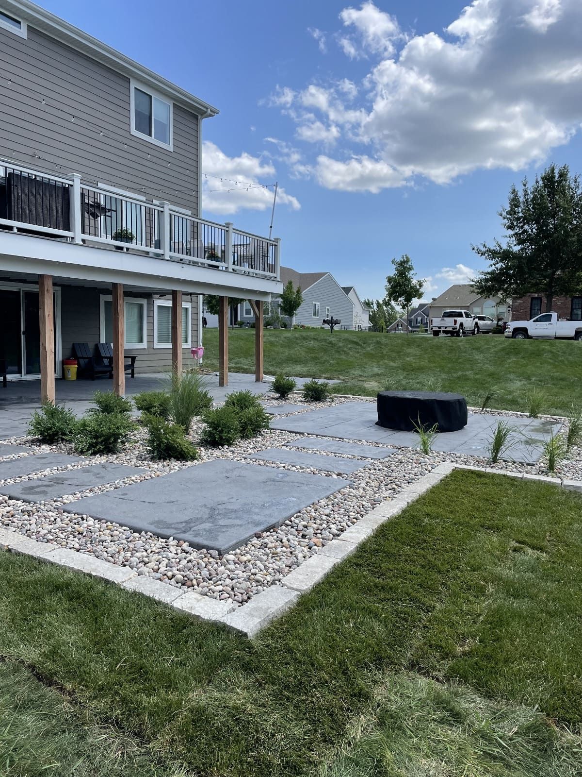 Backyard patio with gray pavers, white rock border, grass, and a deck.