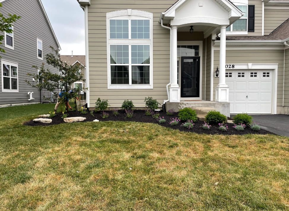 Front of a beige house with landscaped flower bed and dry lawn.