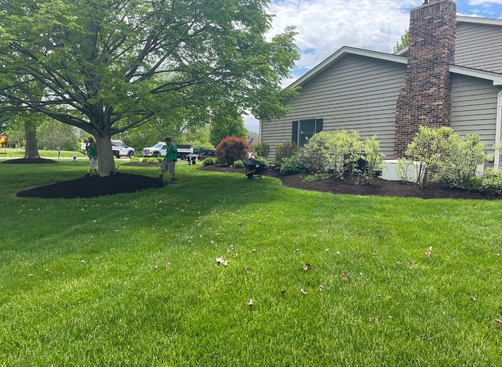 Lawn care workers mulching and mowing residential lawn near a house with a stone chimney.