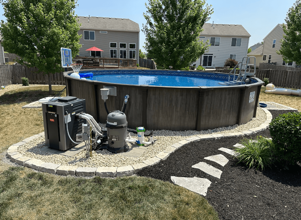 Above-ground pool with equipment in a backyard, surrounded by landscaping and residential homes.