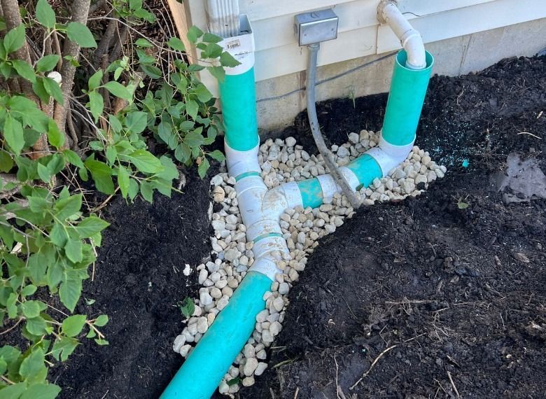 Green drain pipes diverting water, installed on a house foundation, resting on gravel.
