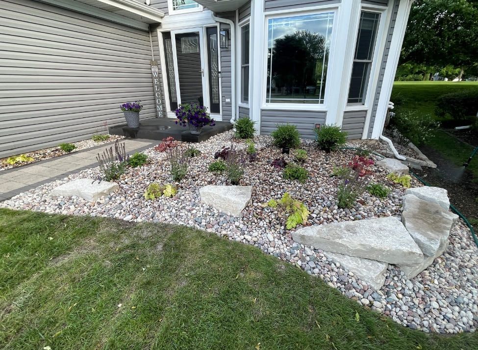 Landscaped front yard with rock bed, plants, and large stones in front of a house.