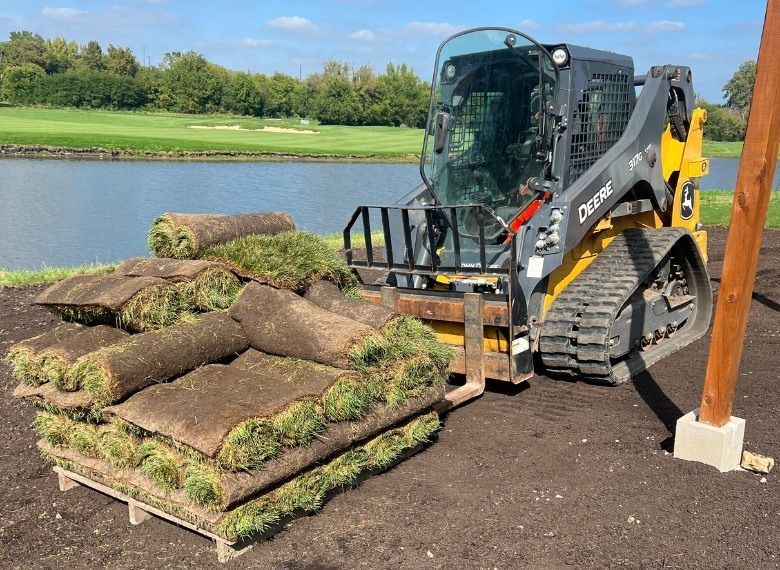 John Deere skid steer carrying pallets of rolled sod on a golf course.