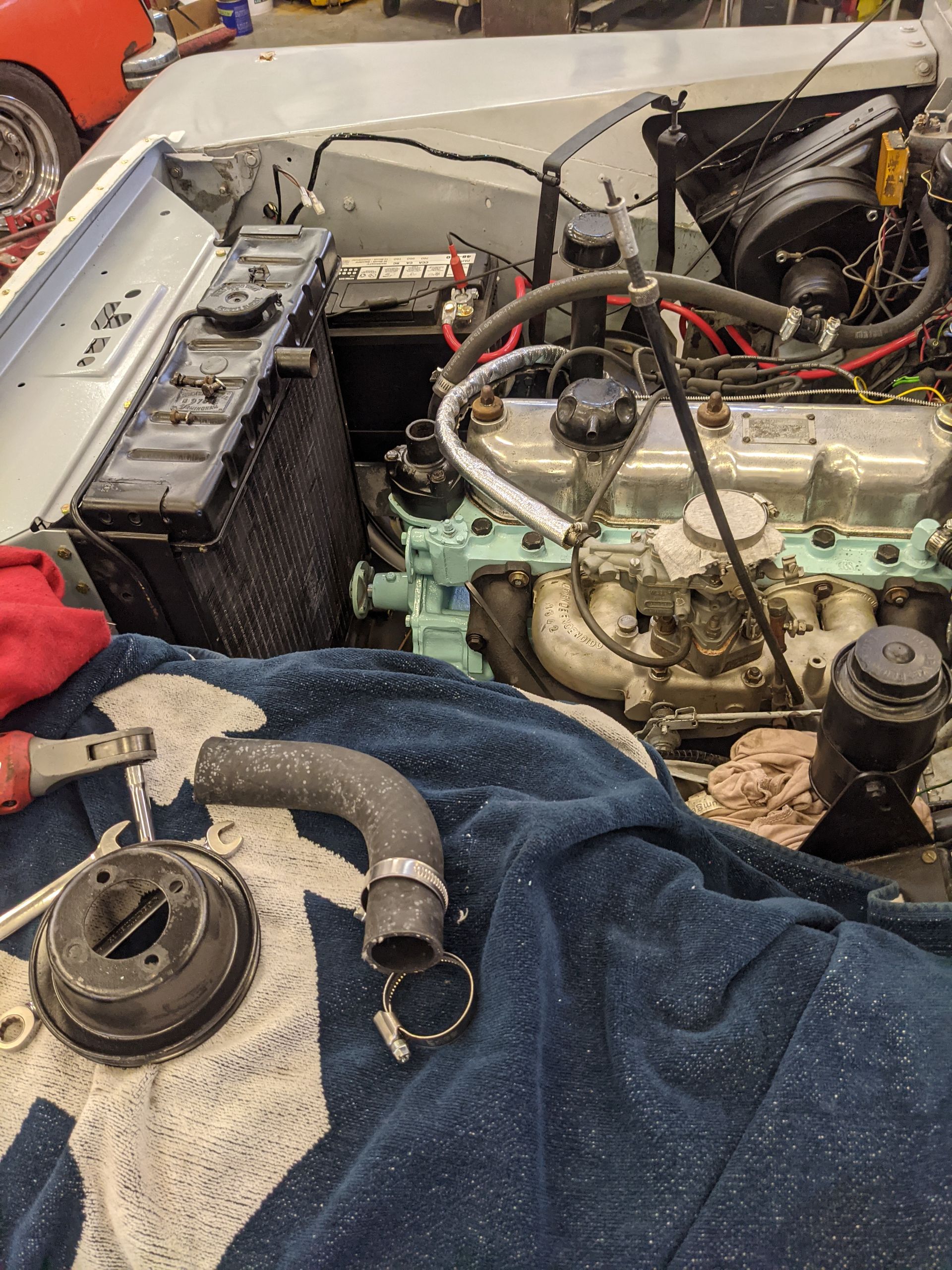 Car engine bay being worked on; old radiator and removed hose visible.
