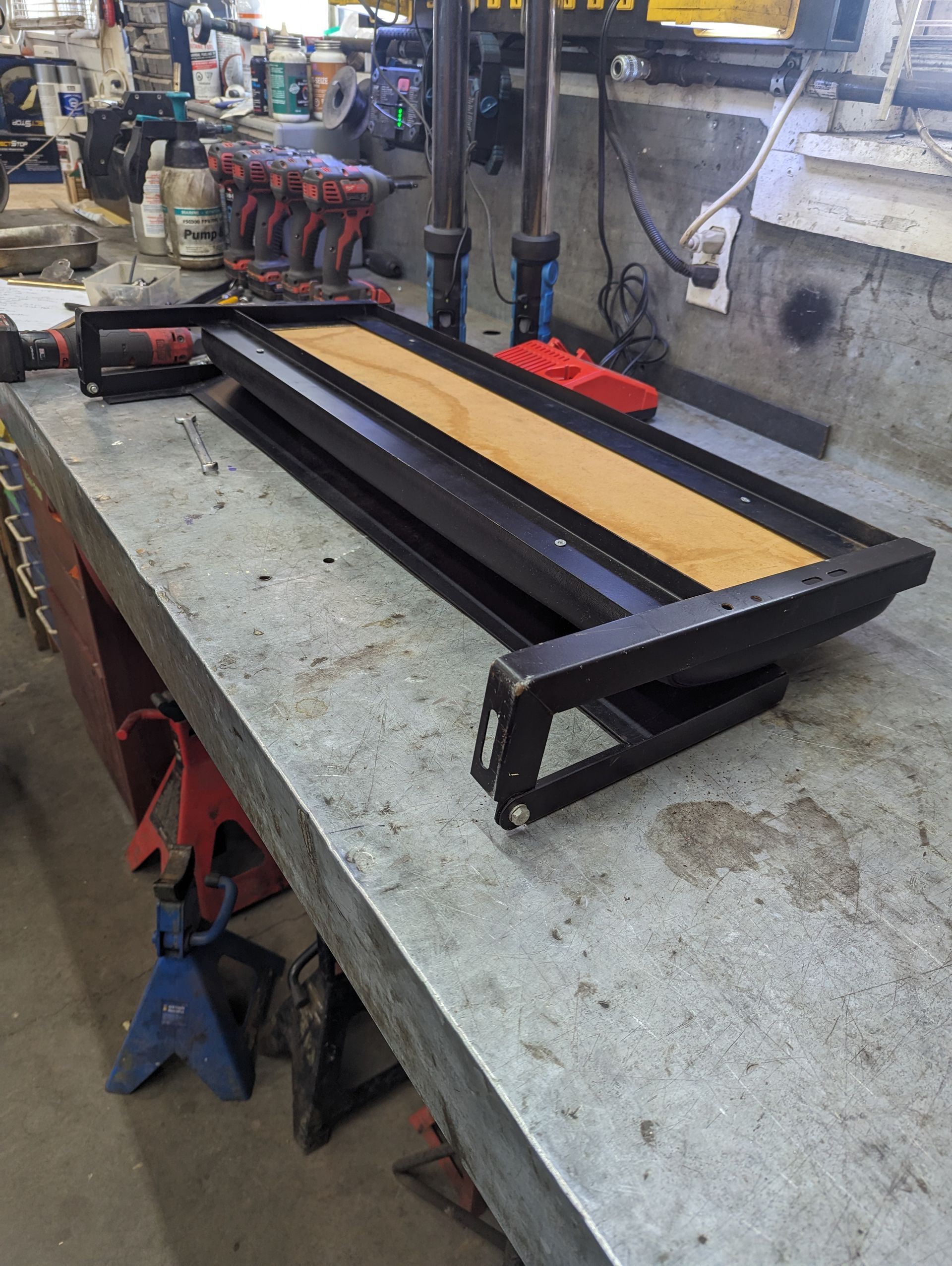 Black metal frame with a wood insert, resting on a workbench. Tools and a jack are nearby.