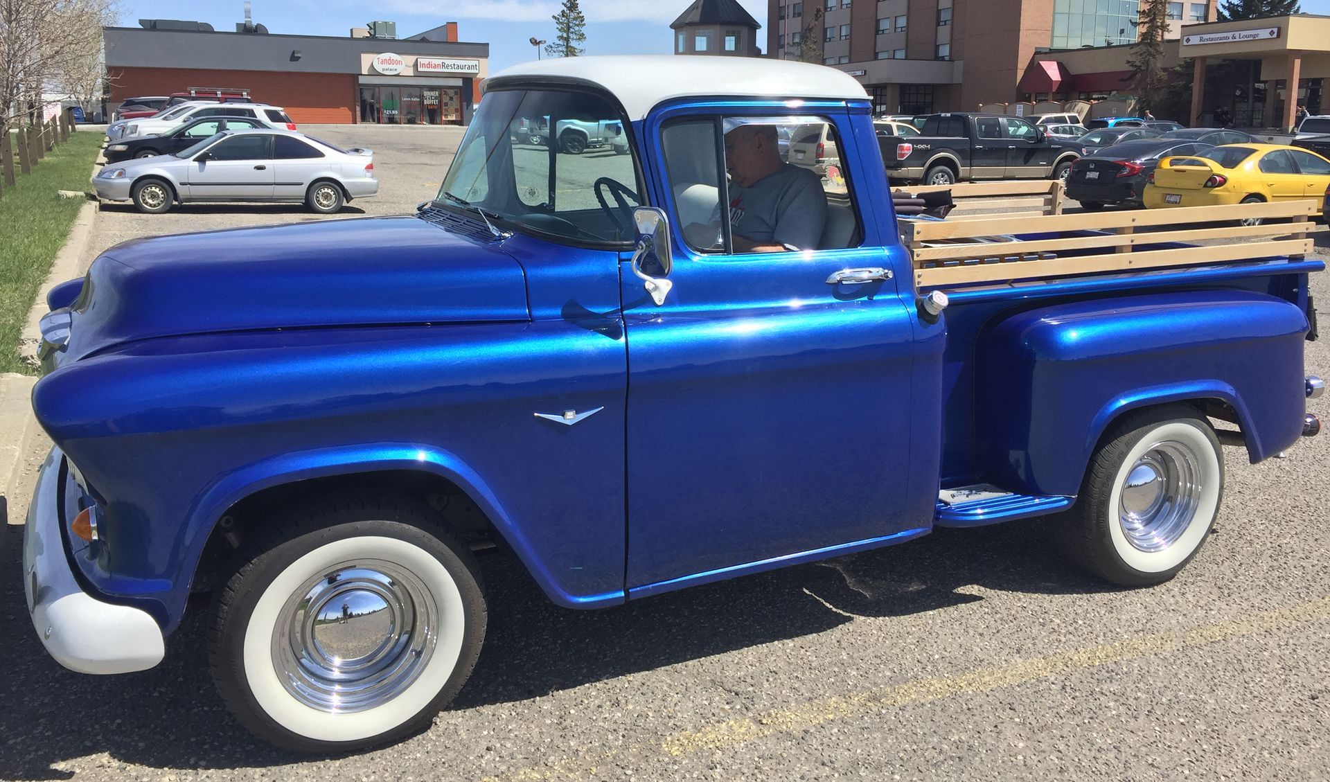 Blue classic pickup truck with white roof and whitewall tires; driver inside.