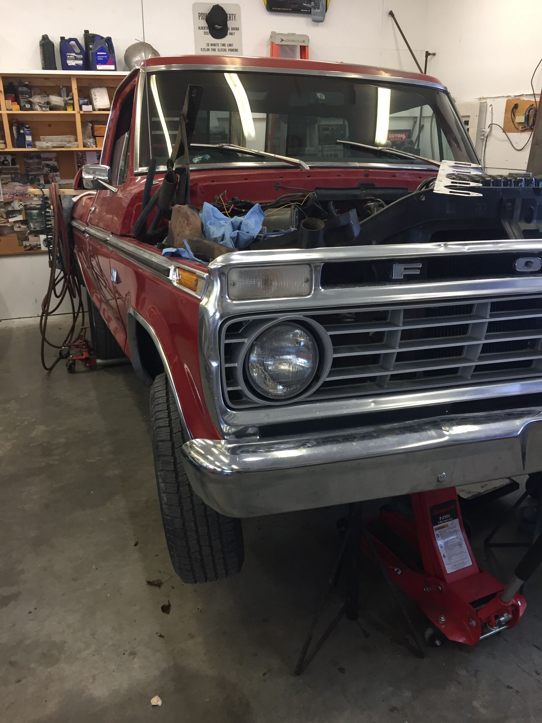 Red Ford pickup truck in a garage, hood open, jacked up.