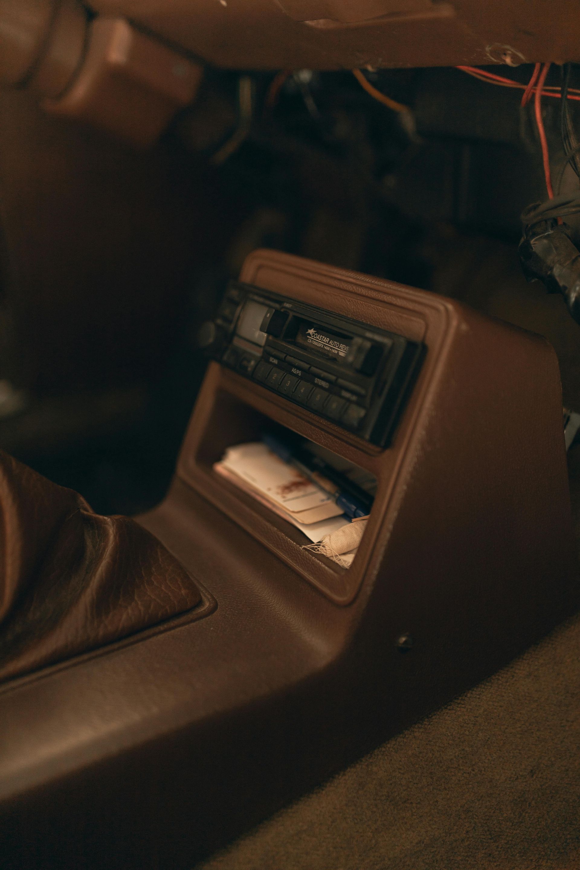 Brown car interior with a cassette player and storage compartment.