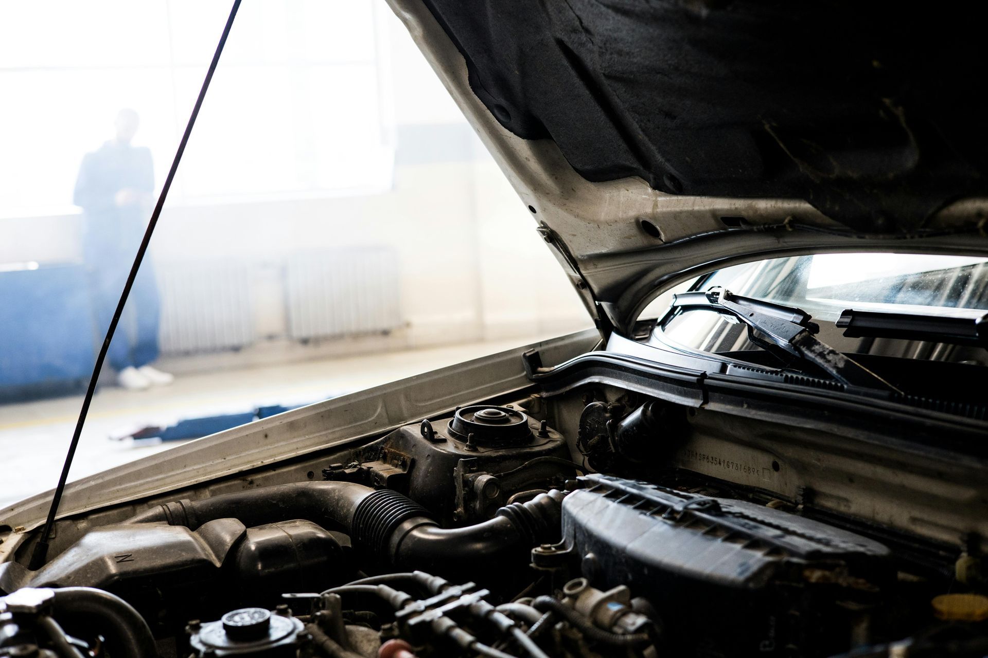 Car engine bay with open hood; mechanic in background, smoke visible.
