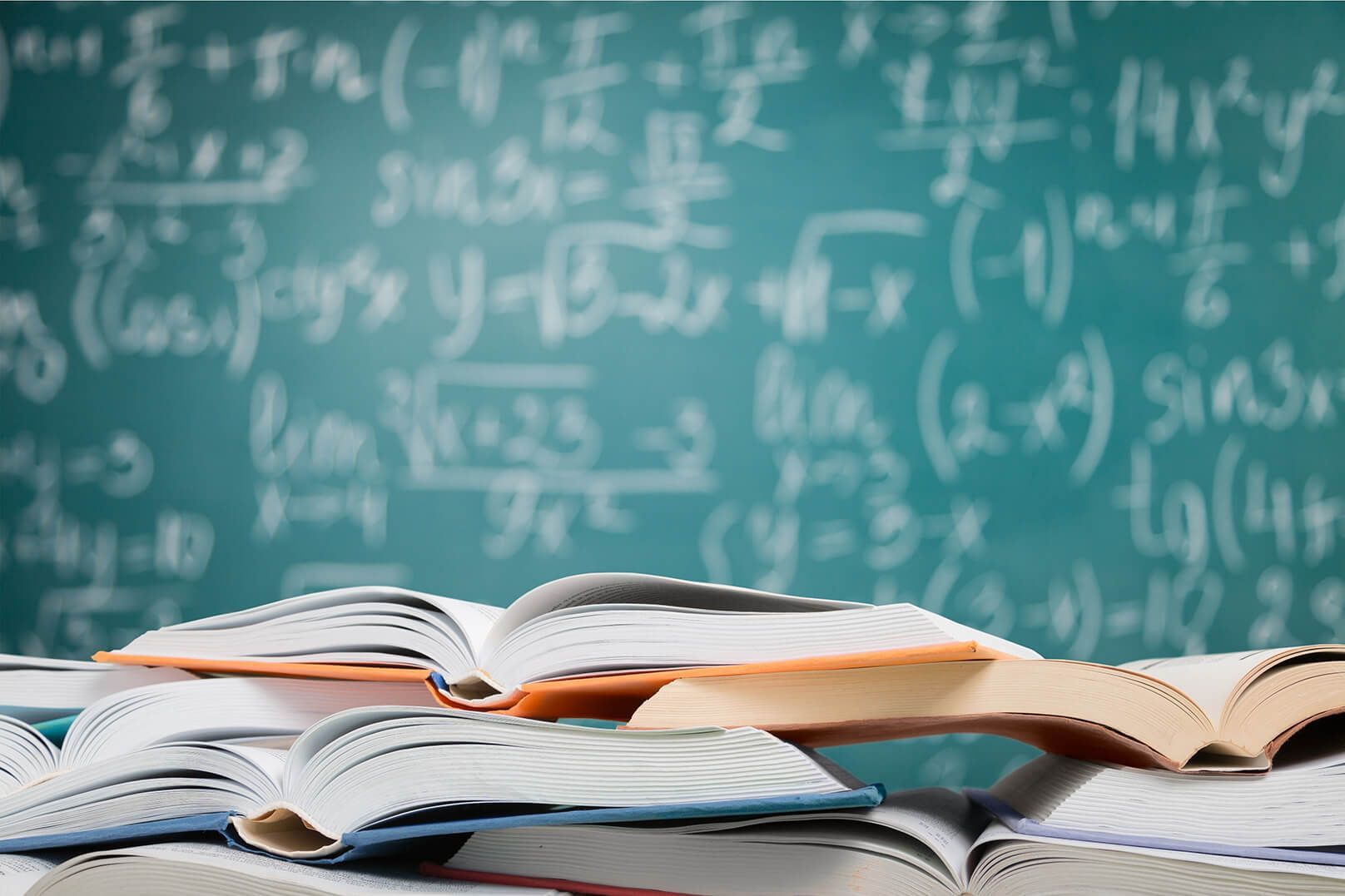 A stack of books in front of a blackboard with math equations on it
